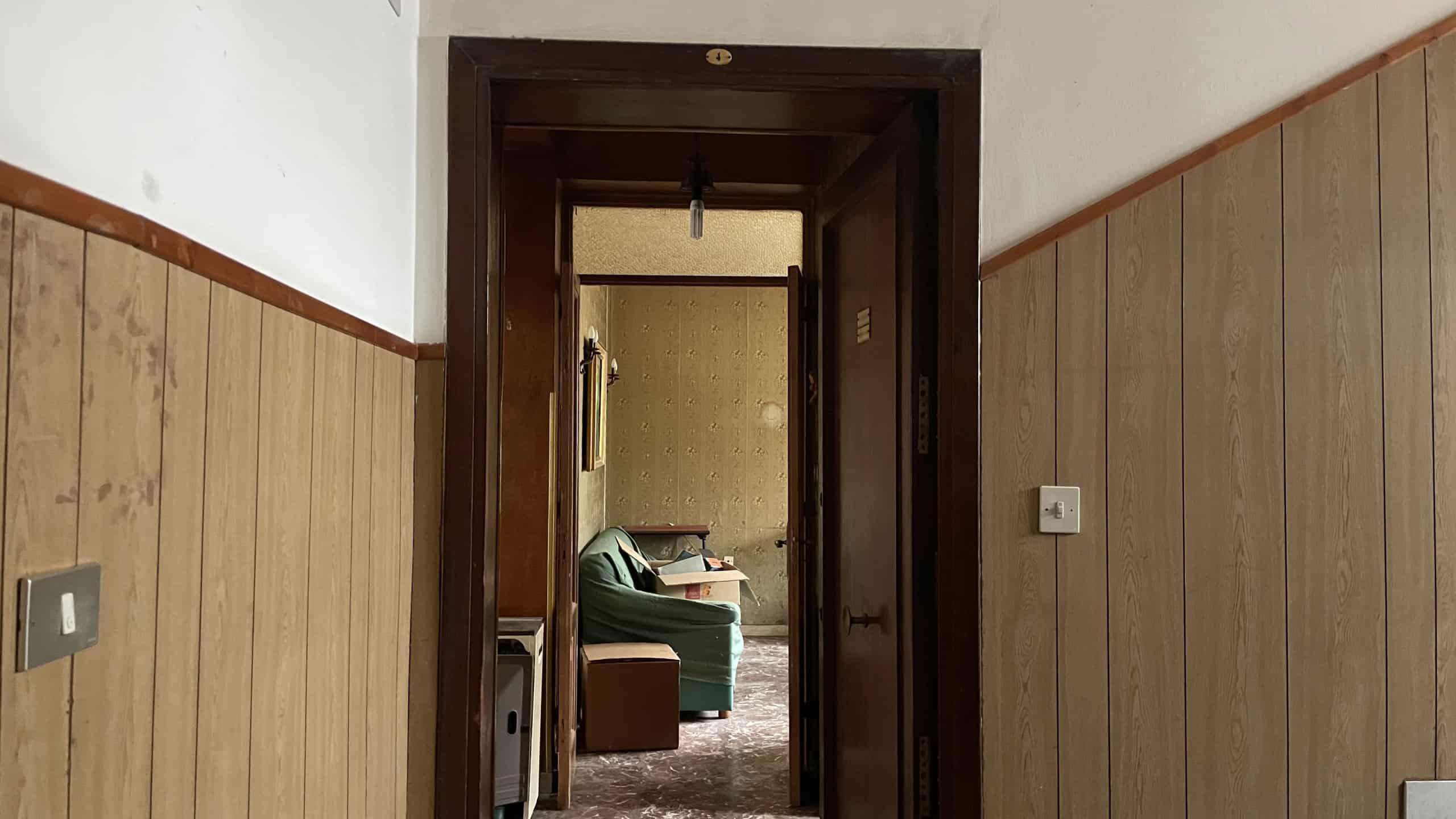 Ampia porta in legno che conduce a un soggiorno con divano e mobili classici, in un ambiente domestico accogliente e ben arredato.