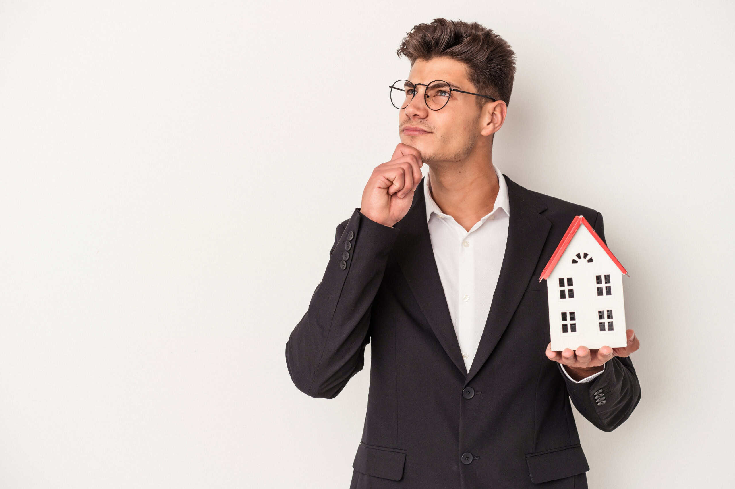 Pensatore con occhiali in abito formale che tiene una casa in miniatura, simbolo di investimento immobiliare o consulenza immobiliare.