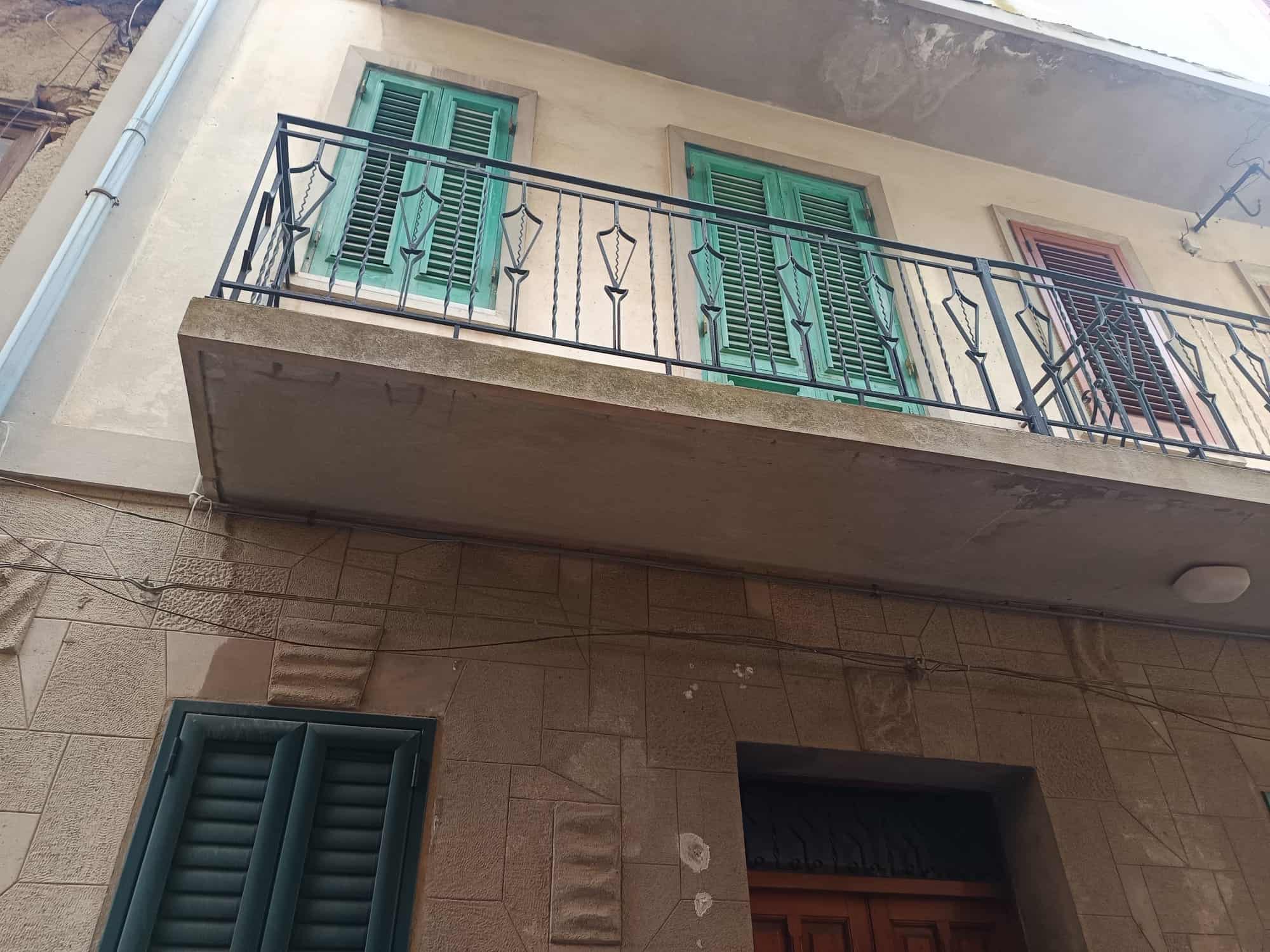 Immagine di una casa con balcone e persiane verdi, situata nel centro storico, con dettagli architettonici in pietra e un balcone in ferro battuto.