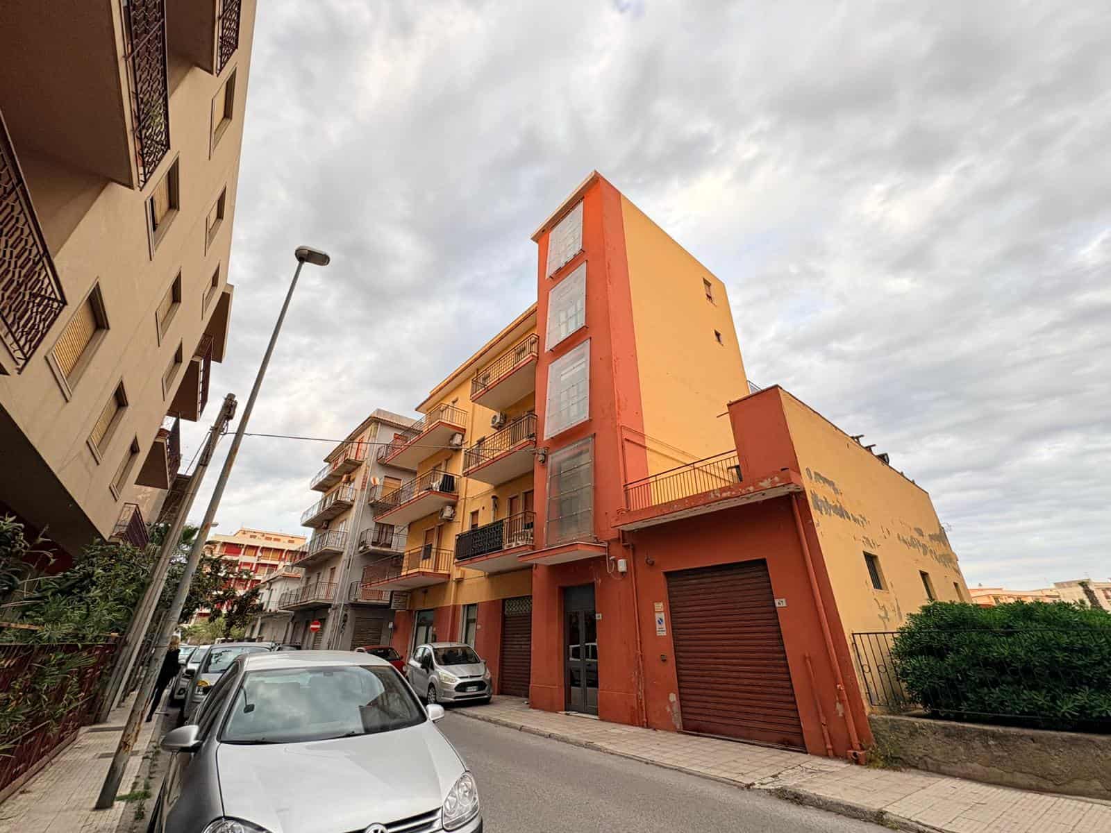 Immagine di un edificio residenziale con facciata arancione e balconi, situato in un quartiere cittadino con auto parcheggiate lungo la strada.