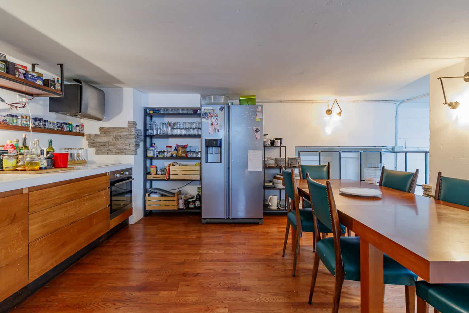 Ampio spazio cucina e sala da pranzo con mobili eleganti, frigorifero e tavolo in legno con sedie blu, ideale per convivialità e cene in famiglia.