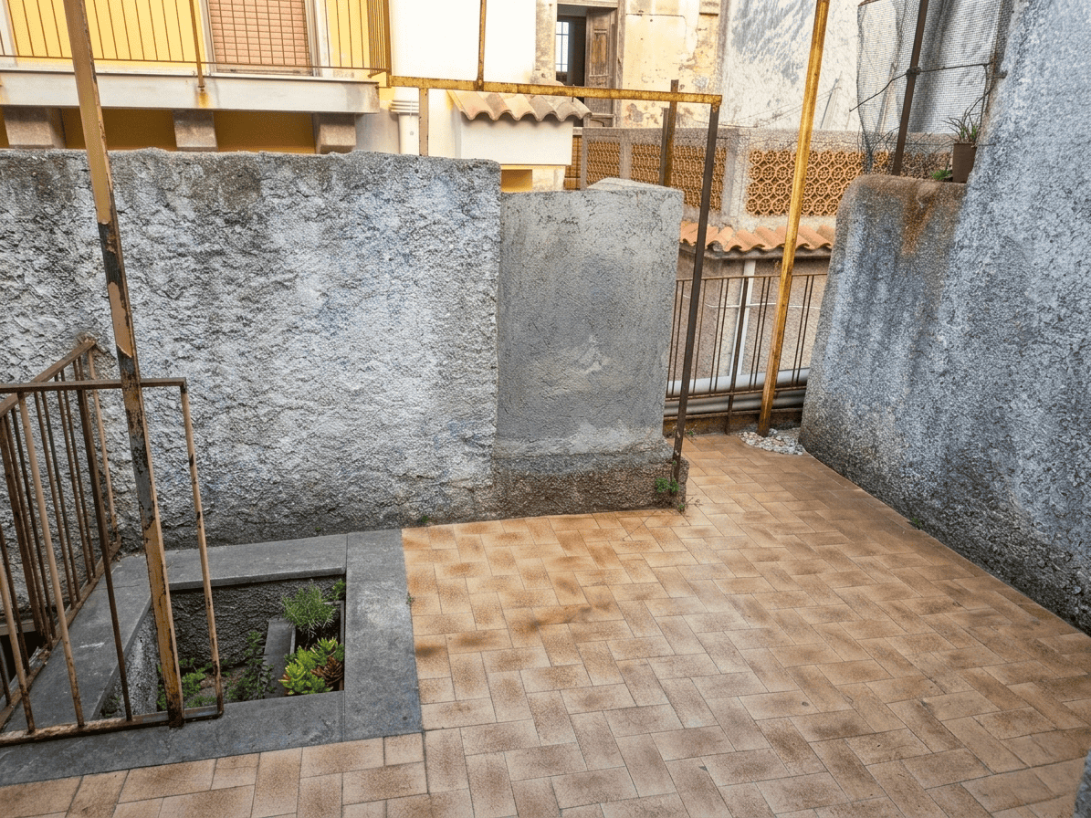 Finestra su un cortile con pavimentazione in mattonelle e muri in pietra, ideale per spazi esterni e relax all'aperto.
