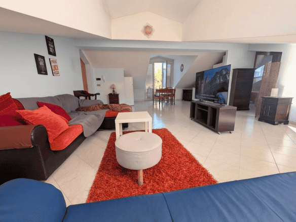 Ampio soggiorno luminoso con divani colorati, TV grande e area relax, arredato con stile moderno e accogliente, ideale per famiglie e amici, con vista sulla zona pranzo e accesso a spazio esterno.