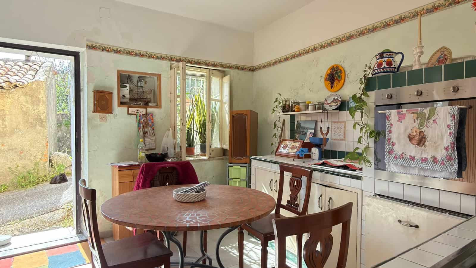 Cucina rustica con mobili vintage, pareti decorate e finestra che lascia entrare luce naturale, atmosfera accogliente e tradizionale.