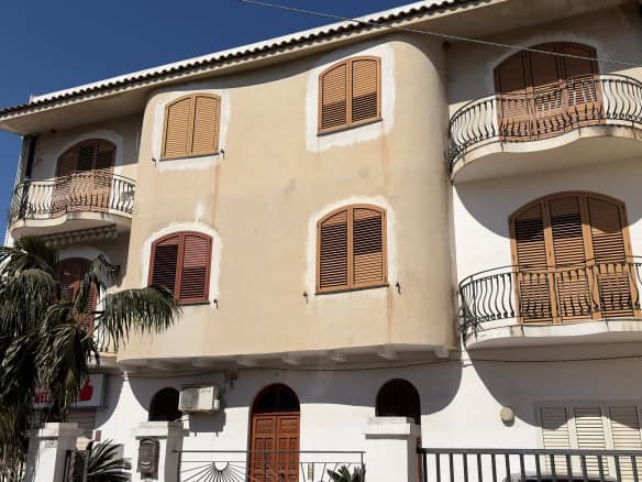 Edificio residenziale con balconi e finestre in stile classico, facciata beige e tetto in tegole, situato in zona urbana soleggiata.