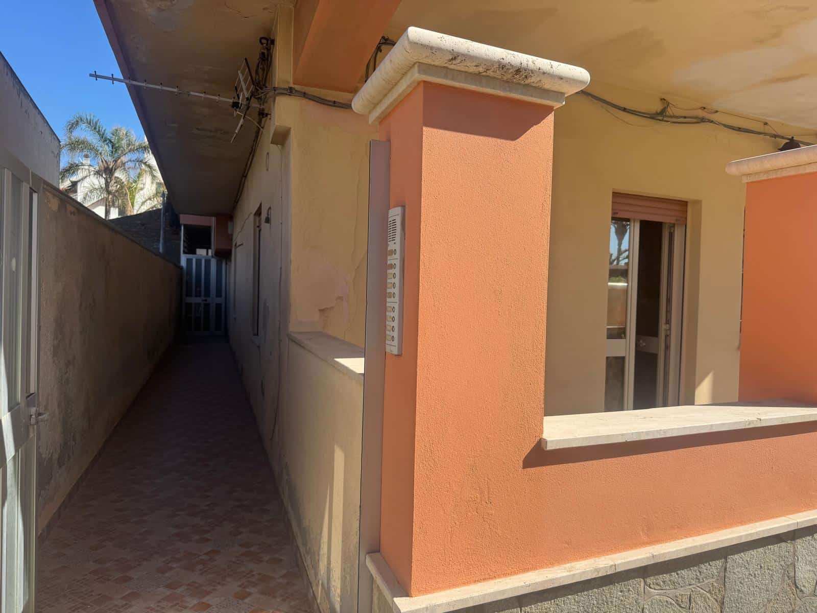 Pannello di controllo elettrico esterno su parete di un appartamento con balcone, vista laterale del corridoio esterno in zona residenziale soleggiata.