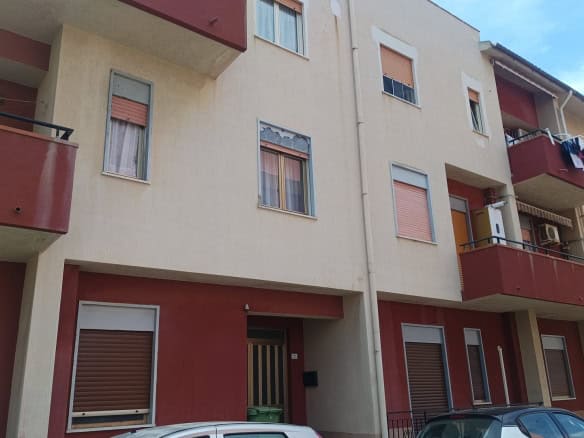 Ampio edificio residenziale con balconi e finestre, facciata in tonalità neutre e dettagli in rosso, parcheggio esterno e ambiente urbano.
