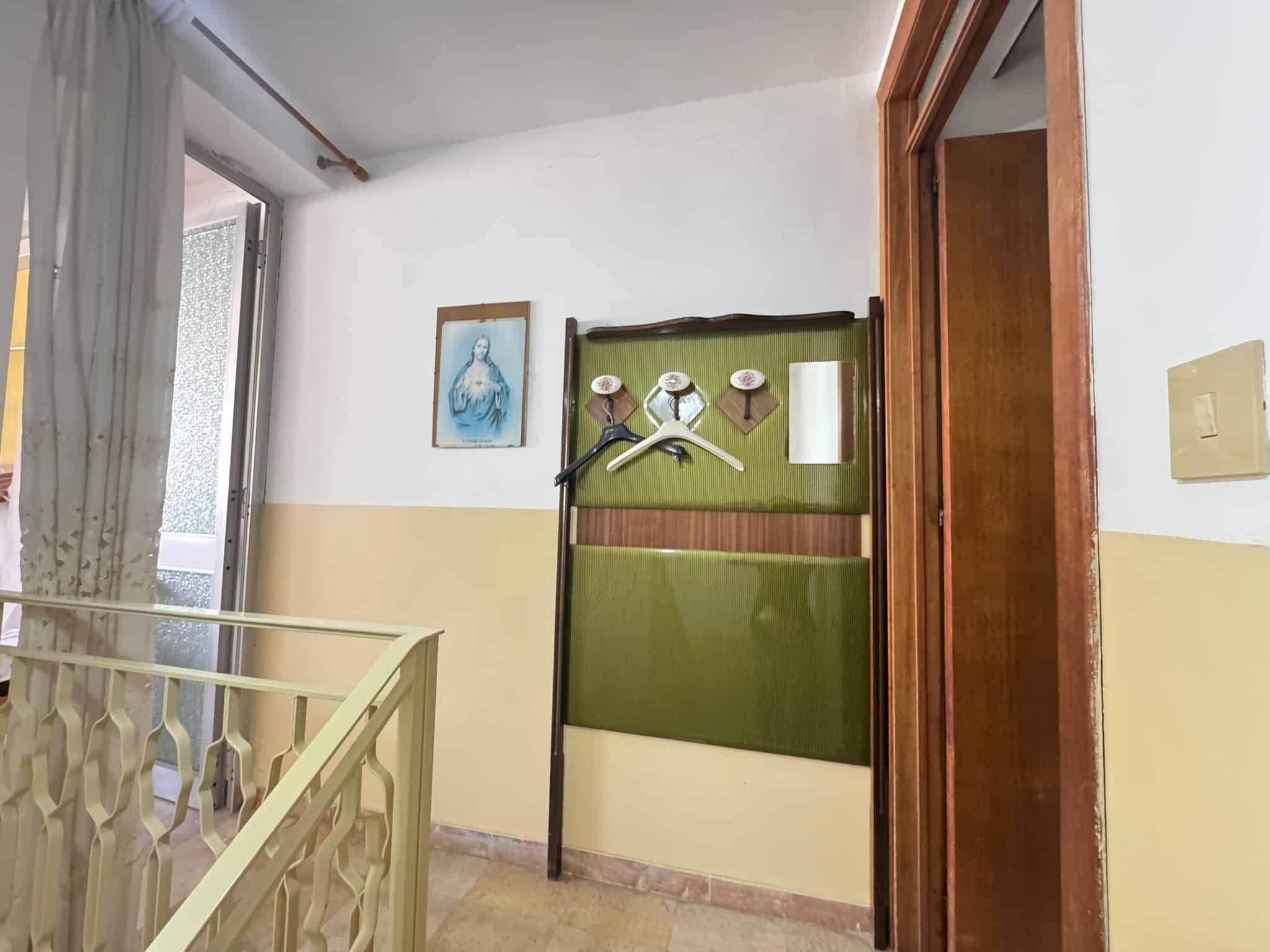 Pannello portaoggetti con ganci e specchio in un ingresso di casa, decorato con quadro e tende leggere, illuminato dalla luce naturale proveniente dalla finestra.