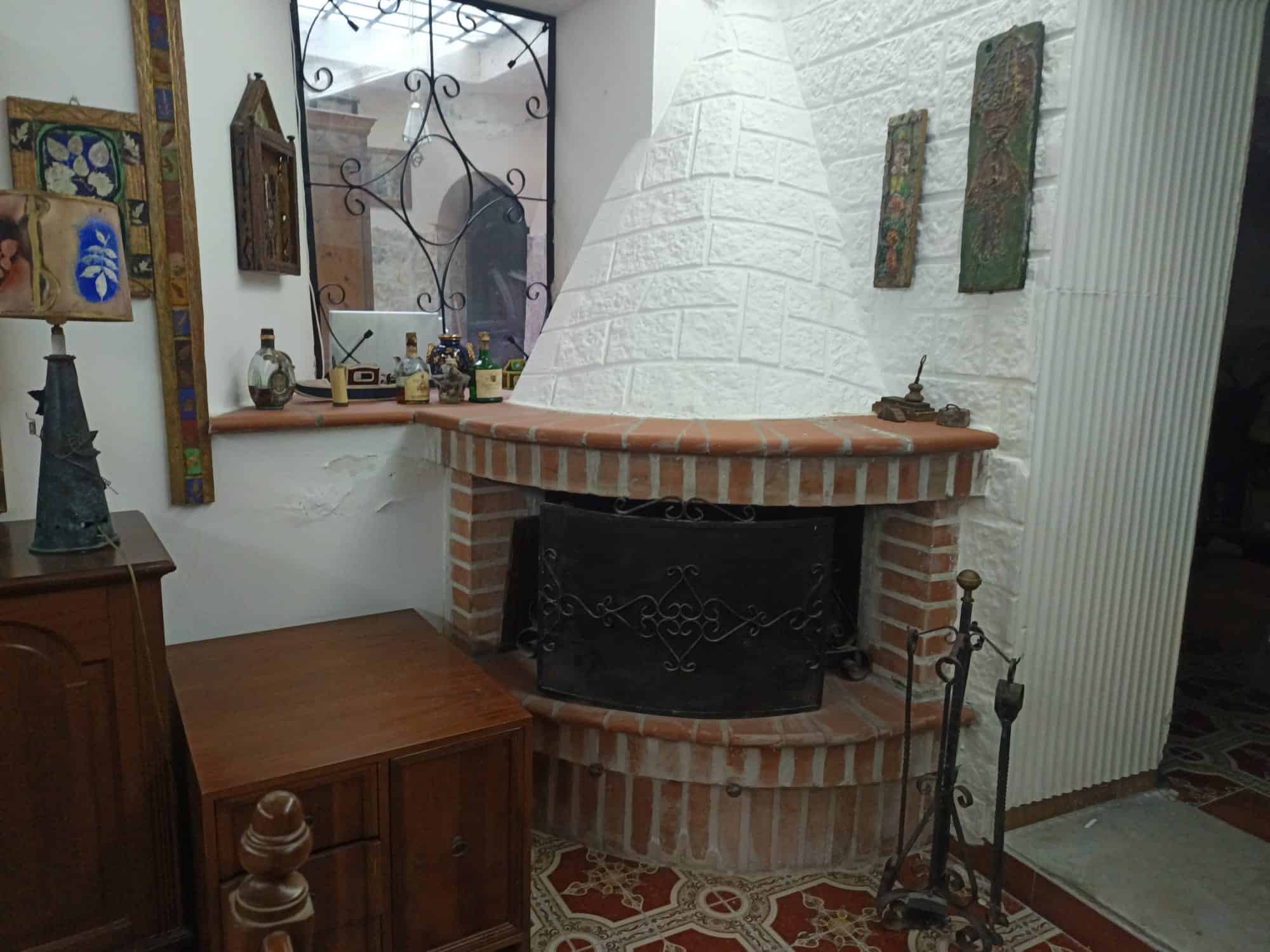 Camino in mattoni rossi con rivestimento in pietra bianca, decorato con oggetti d'antiquariato e quadri artistici, in un ambiente accogliente e rustico.