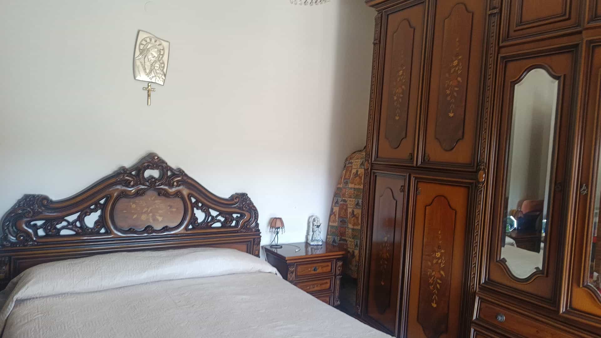 Lettino matrimoniale con testiera in legno intagliato, camera da letto classica con armadio in legno e dettagli decorativi eleganti.