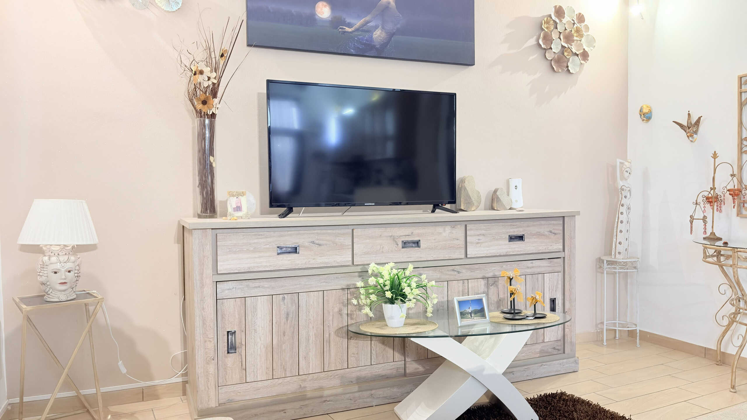 Elegante mobile TV in stile shabby chic con finitura bianca, posizionato in soggiorno luminoso con decorazioni floreali e oggetti d'arredo raffinati.