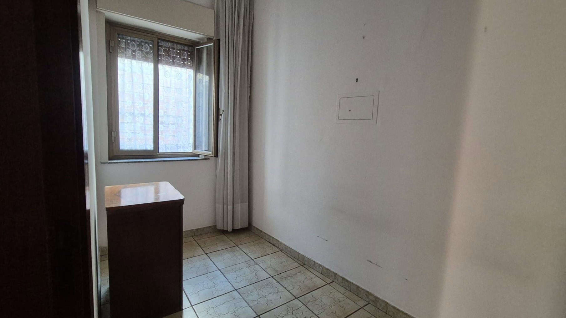 Appartamento vuoto con finestra e pavimento in piastrelle, vista interna di una stanza in affitto o vendita.