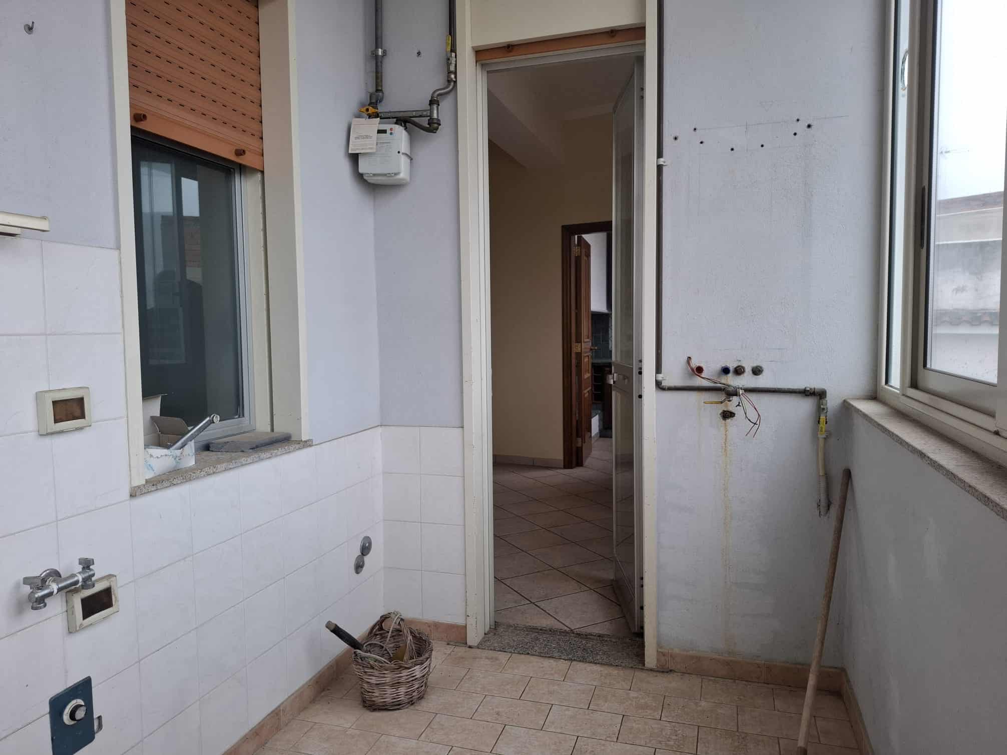 Lavanderia in fase di ristrutturazione con pareti bianche, piastrelle beige e grandi finestre che lasciano entrare molta luce naturale, pronta per essere rinnovata e personalizzata.