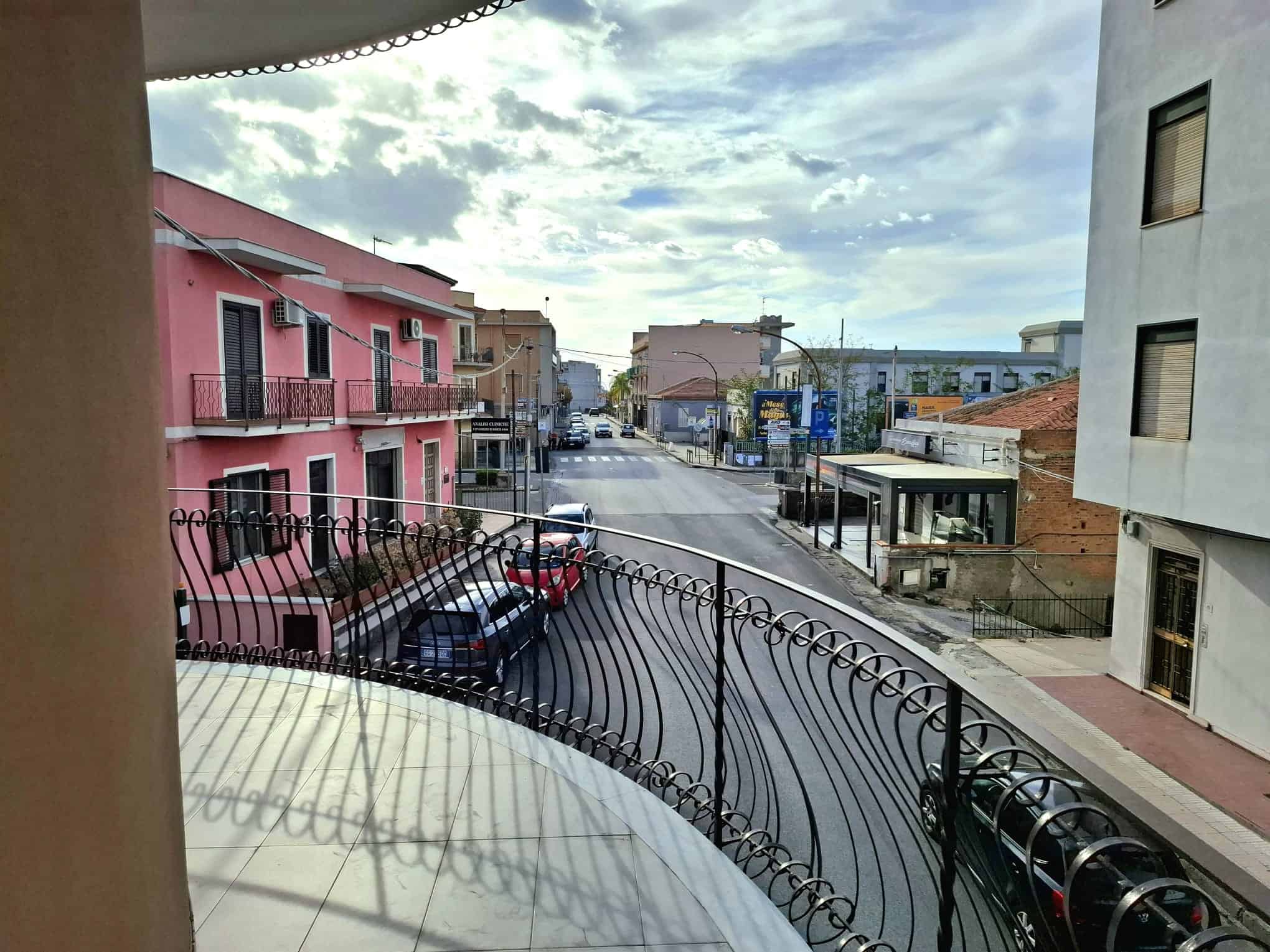 Vista panoramica di una strada urbana con edifici colorati e cielo nuvoloso, vista dal balcone di un appartamento a NextCasa.