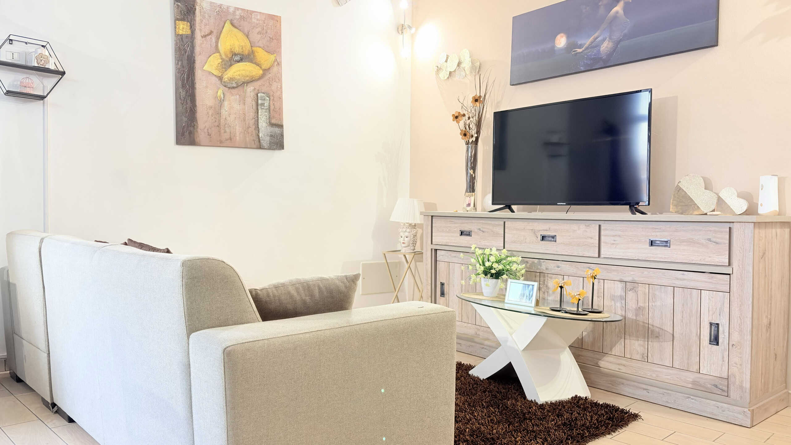 Elegante soggiorno con divano beige, TV a schermo piatto e arredi moderni, ideale per vivere momenti di relax e intrattenimento in un ambiente accogliente e ben arredato.
