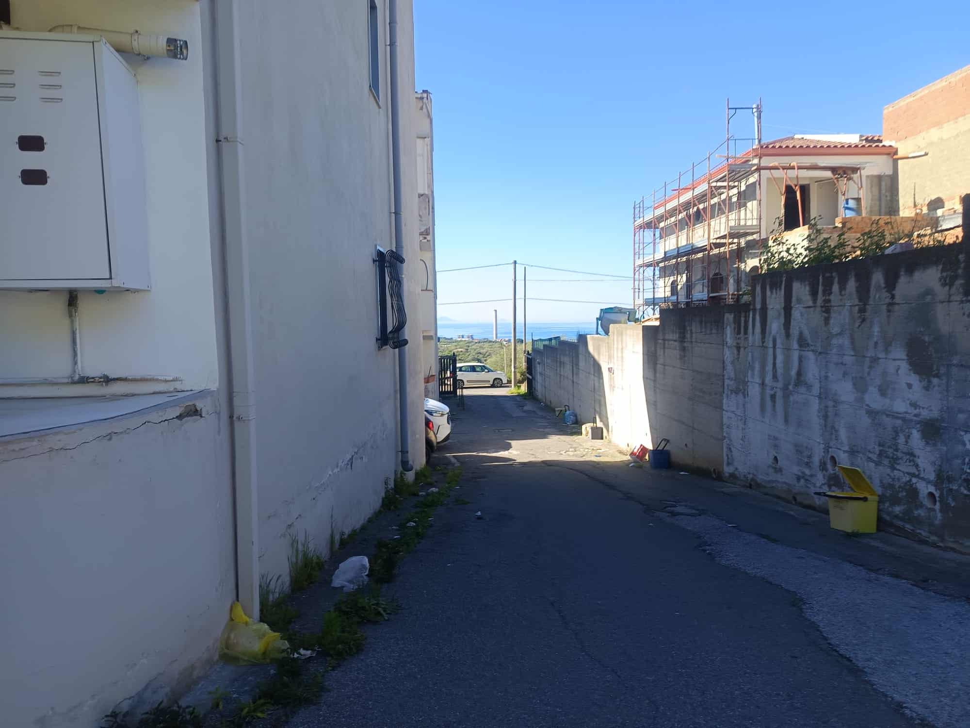 Vicolo stretto tra edifici con vista sul mare in lontananza, in zona residenziale di NextCasa, Italia.
