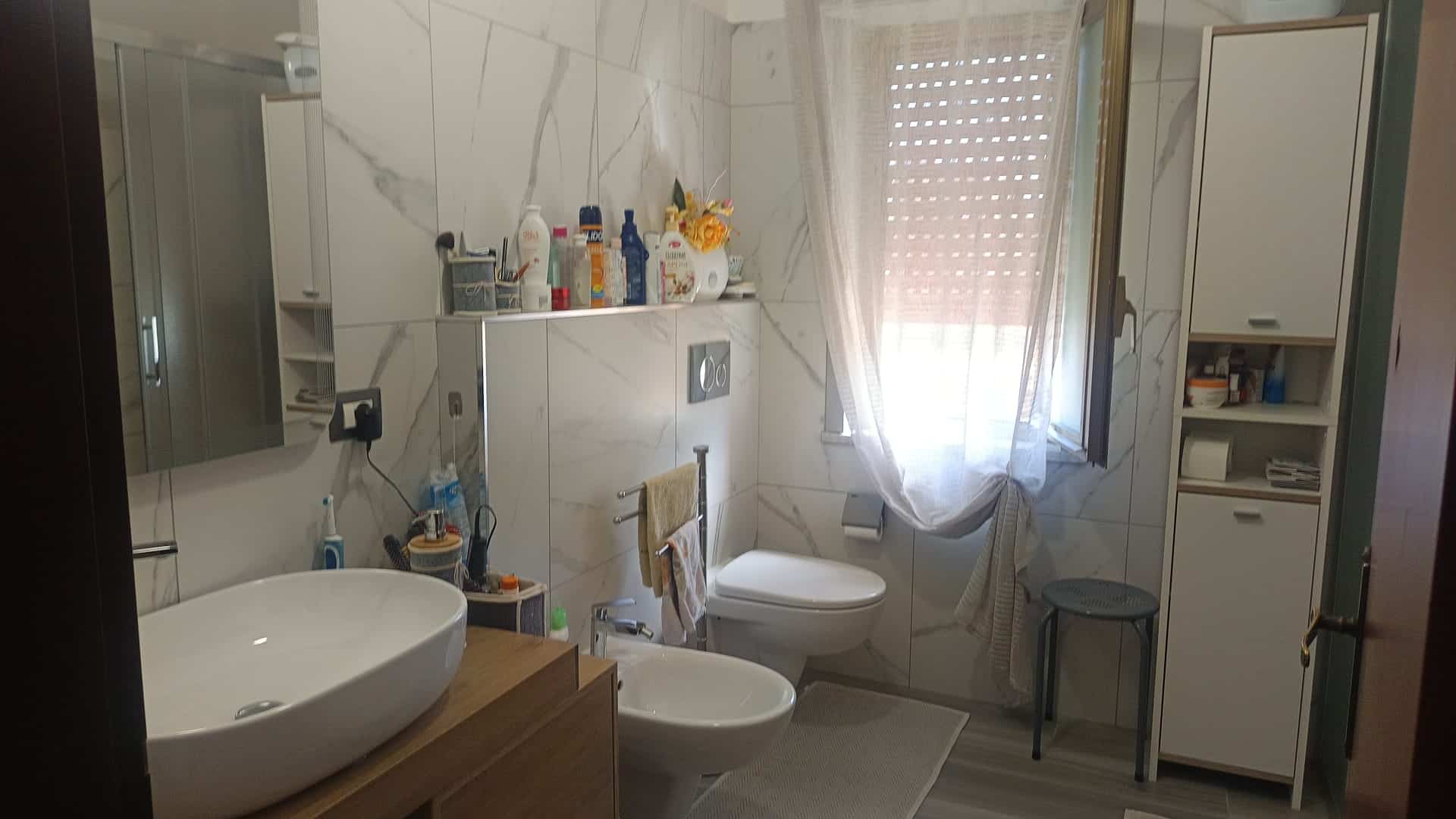 Lavabo e servizi igienici in bagno con arredi moderni, finestra con tende leggere, spazio funzionale e luminoso, ideale per case e appartamenti in vendita o affitto.