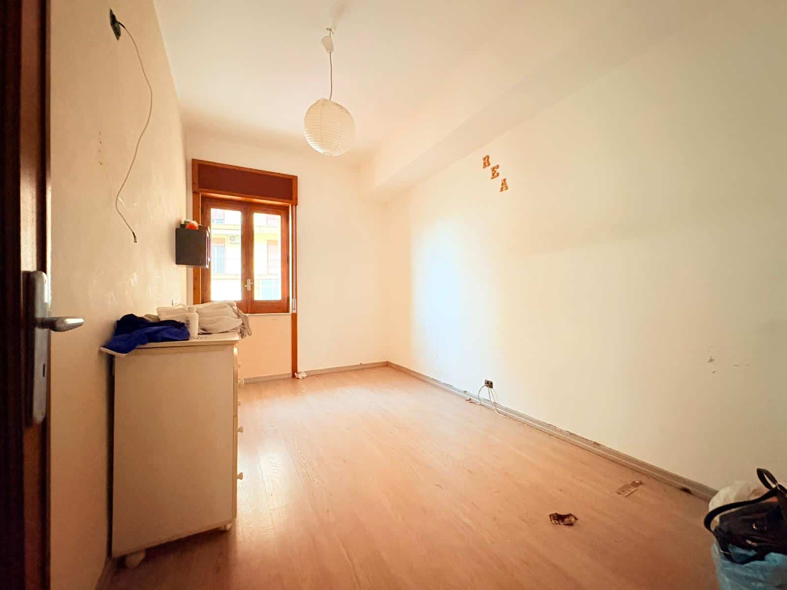 Stanza vuota con pareti bianche, finestra in legno e pavimento in parquet, pronta per essere arredata e personalizzata.