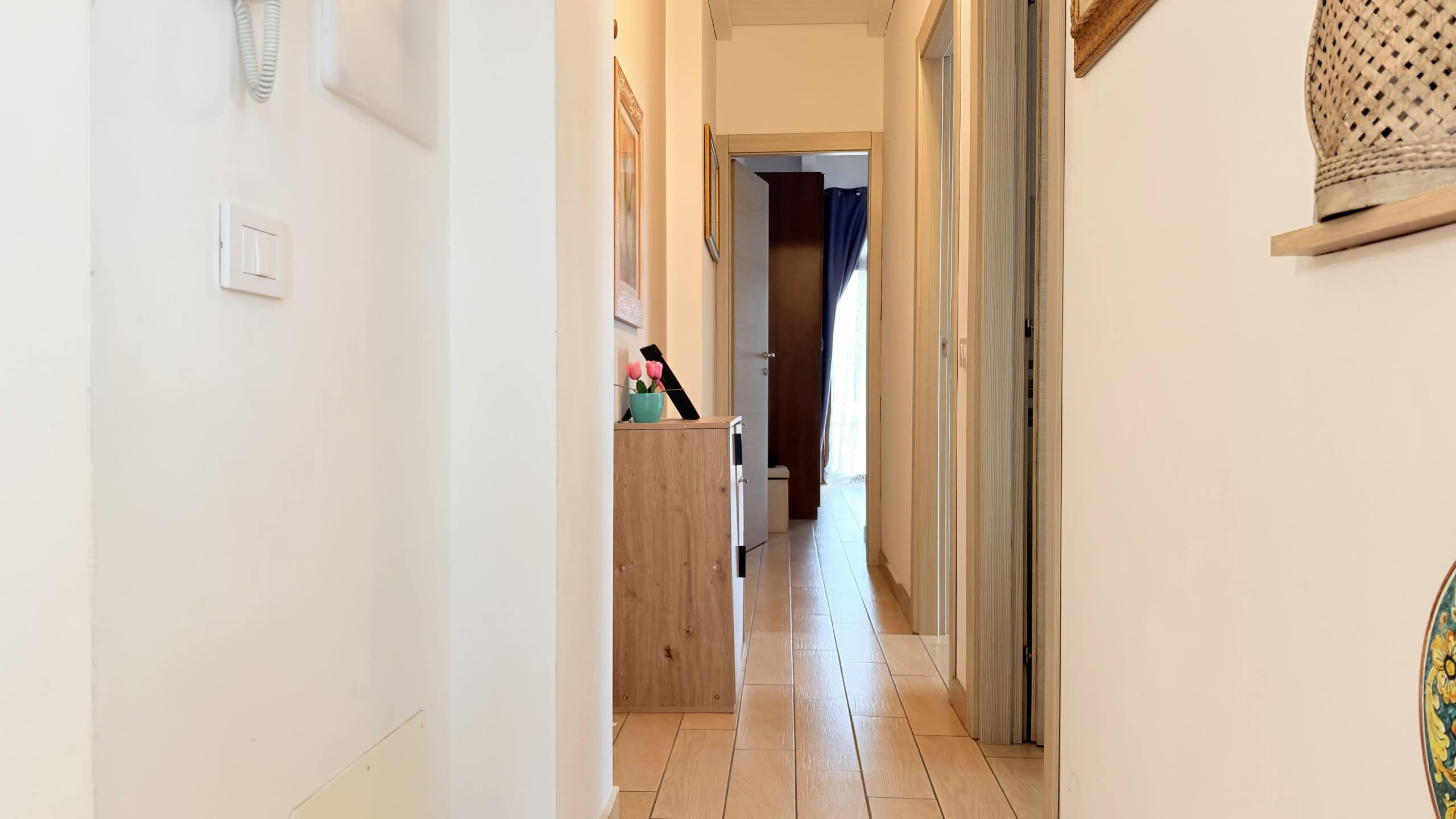 Elegante corridoio interno di un appartamento con pavimento in legno chiaro, pareti bianche e decorazioni moderne, ideale per case in vendita o in affitto.