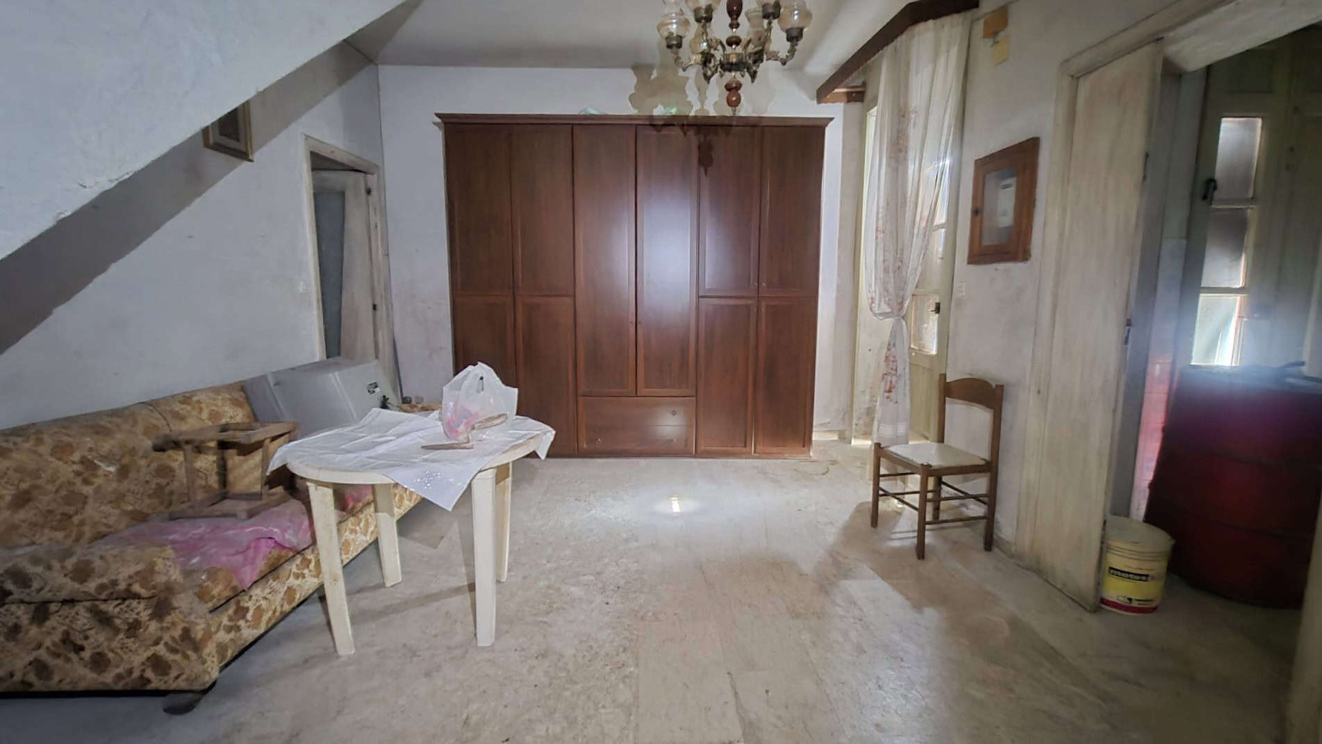 Antico soggiorno con mobili vintage, divano e armadio in legno, illuminato da luce naturale e lampadario d'epoca, in un ambiente accogliente e caratteristico.