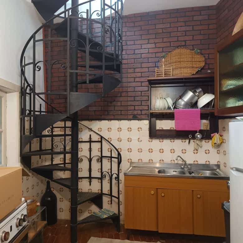Esterno di una cucina compatta con scala a chiocciola in ferro battuto, pareti in mattoni rossi e mobili in legno, ideale per spazi abitativi funzionali e moderni.