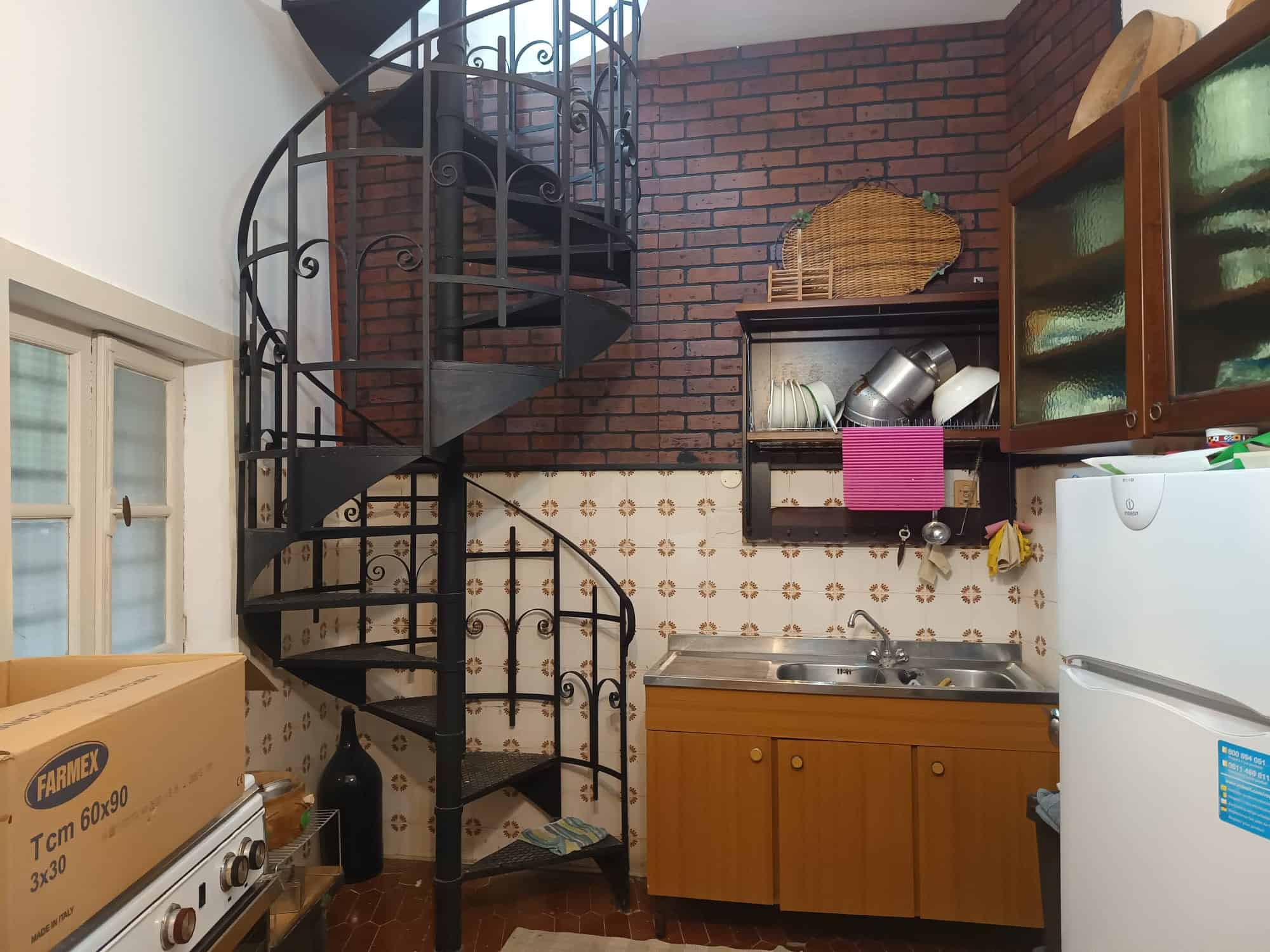 Esterno di una cucina compatta con scala a chiocciola in ferro battuto, pareti in mattoni rossi e mobili in legno, ideale per spazi abitativi funzionali e moderni.