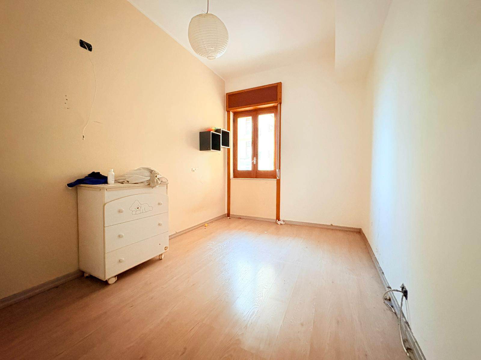 Appartamento vuoto con pareti chiare, finestra grande e pavimento in legno, pronto per essere arredato e personalizzato. Ideale per chi cerca una soluzione abitativa luminosa e spaziosa.