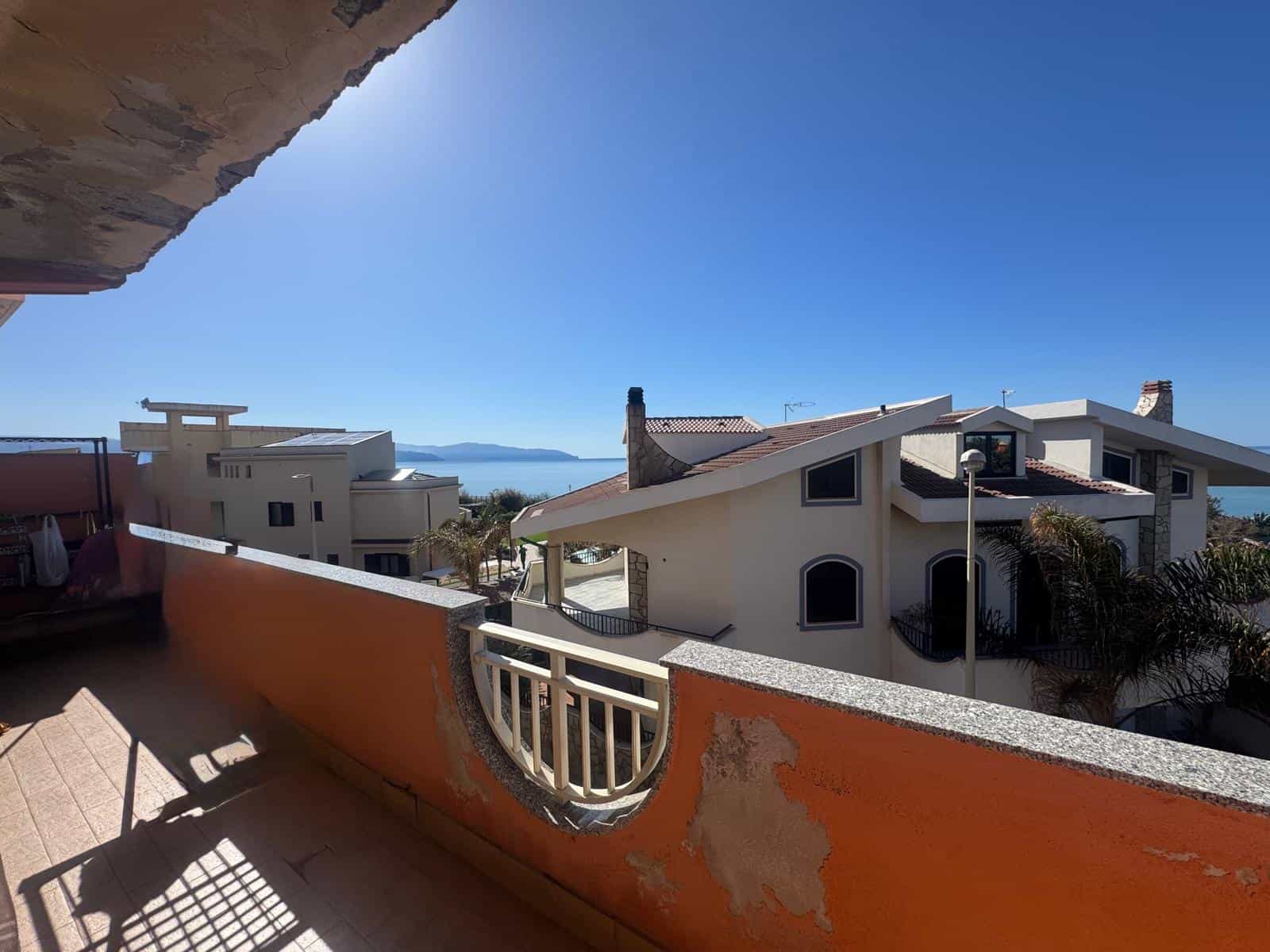 Vista panoramica di case moderne e di un mare in lontananza, vista da un balcone soleggiato in un quartiere residenziale.