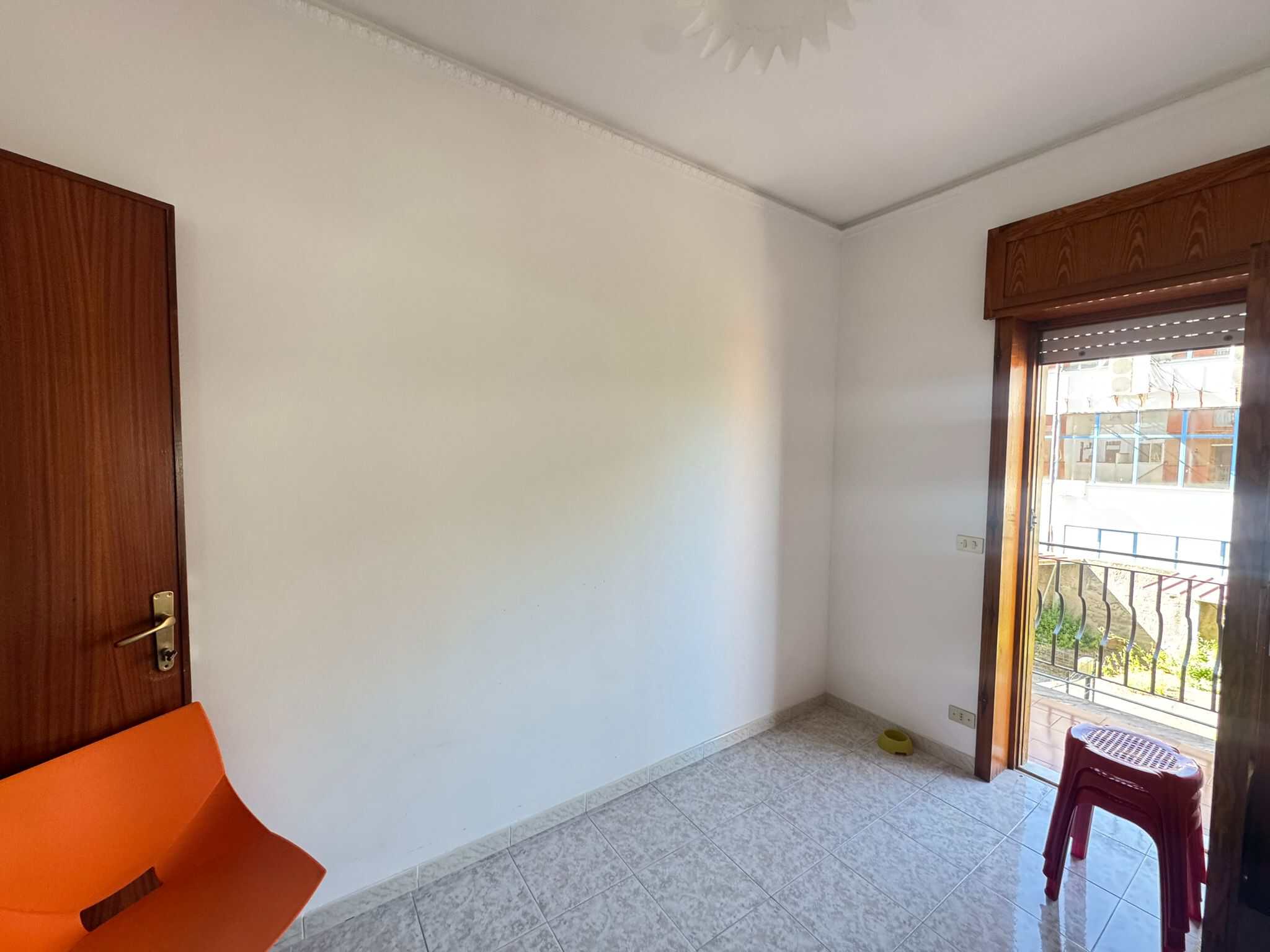 Camera da letto vuota con pareti bianche, pavimento in piastrelle e balcone con vista urbana, ideale per appartamenti in vendita o affitto.