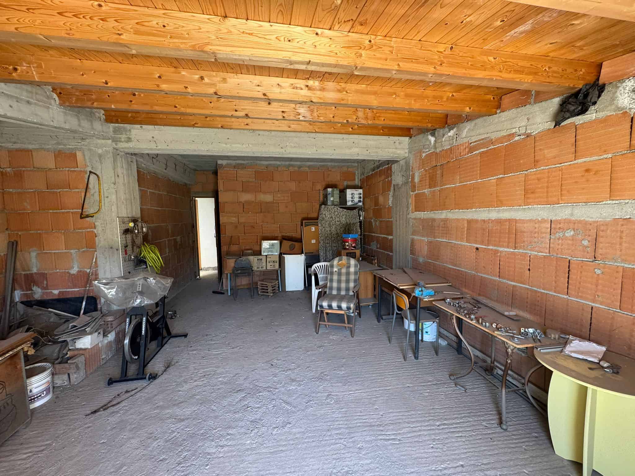 Pannello di costruzione di un garage o magazzino in fase di finitura, con pareti in mattoni rossi e soffitto in legno, spazio aperto con mobili e attrezzature di lavoro.