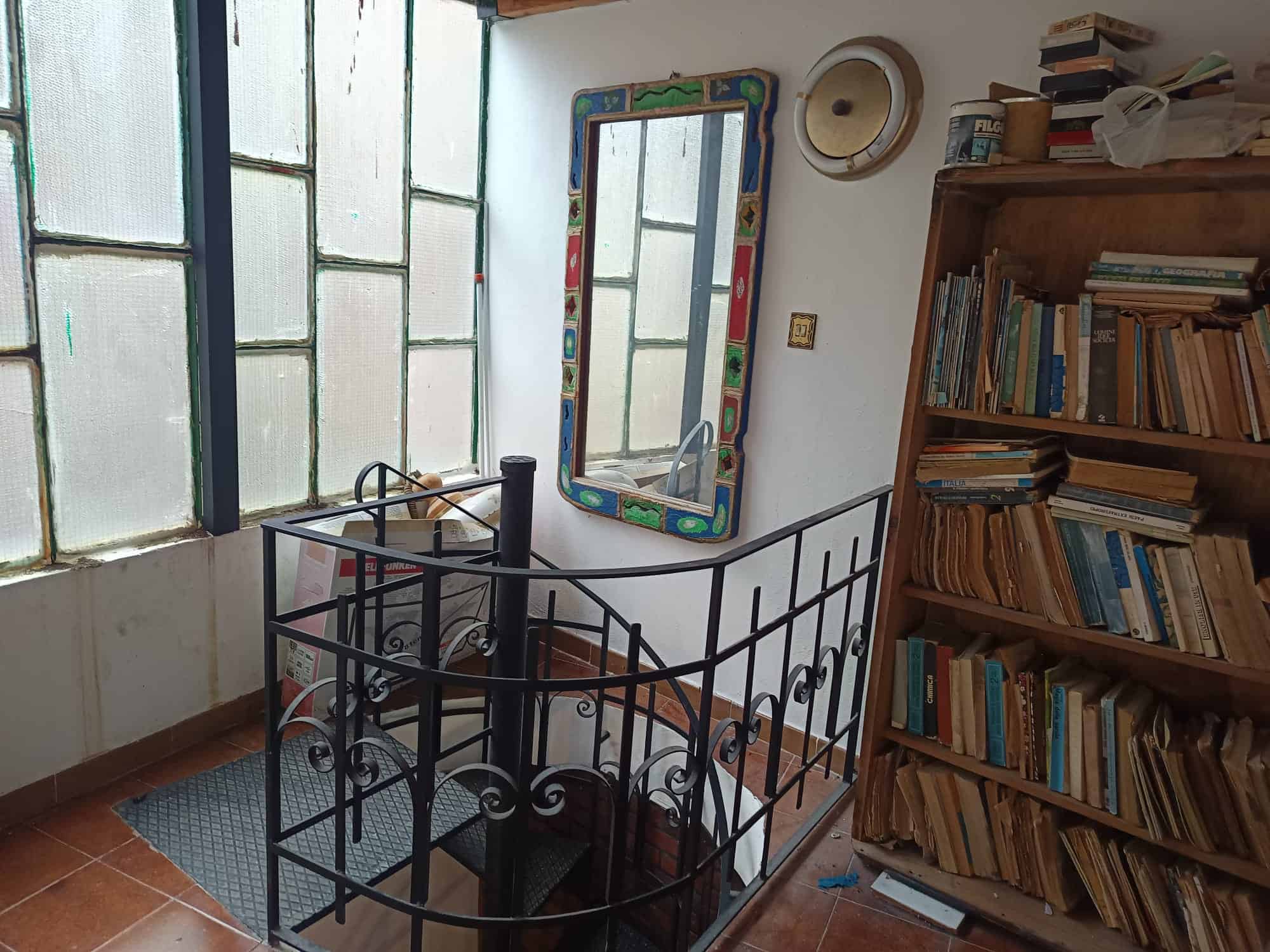 Scala interna in ferro battuto con ringhiera decorativa, in un ambiente domestico con libreria e finestra grande, stile semplice e funzionale.
