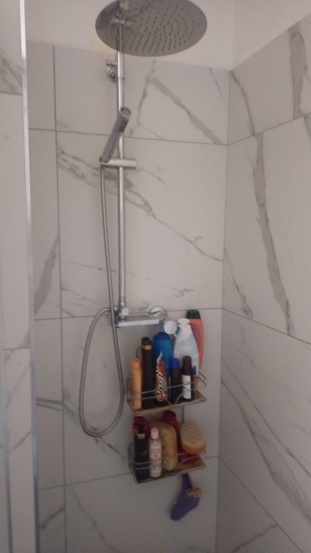 Doccia moderna con soffitto piastrellato in marmo bianco, accessori per bagno con prodotti per la cura personale e spugne, ambiente elegante e funzionale.