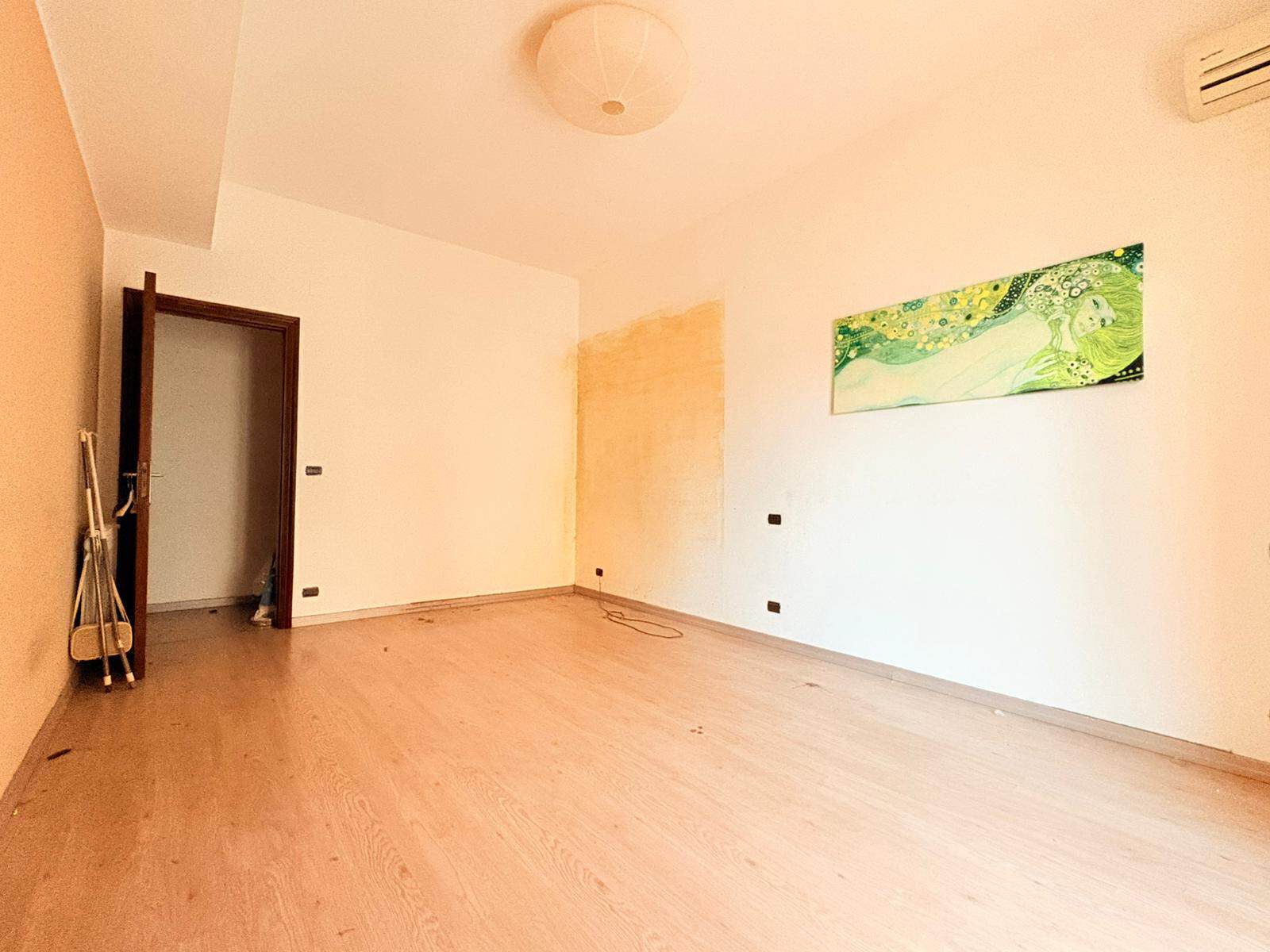 Interno di un appartamento vuoto con pareti bianche, pavimento in legno chiaro e aria condizionata, ideale per ristrutturazione o arredamento personalizzato.