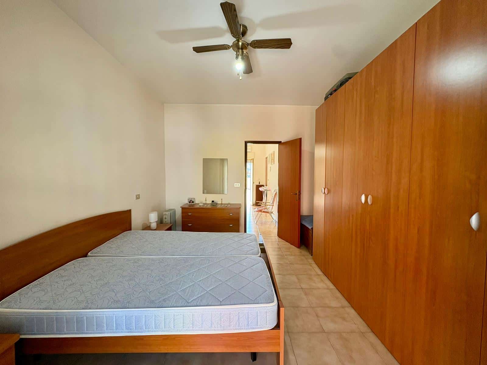 Letto matrimoniale con armadio a muro in una camera da letto luminosa e spaziosa, con pareti bianche e pavimento in ceramica, ideale per affitti o acquisti immobiliari.