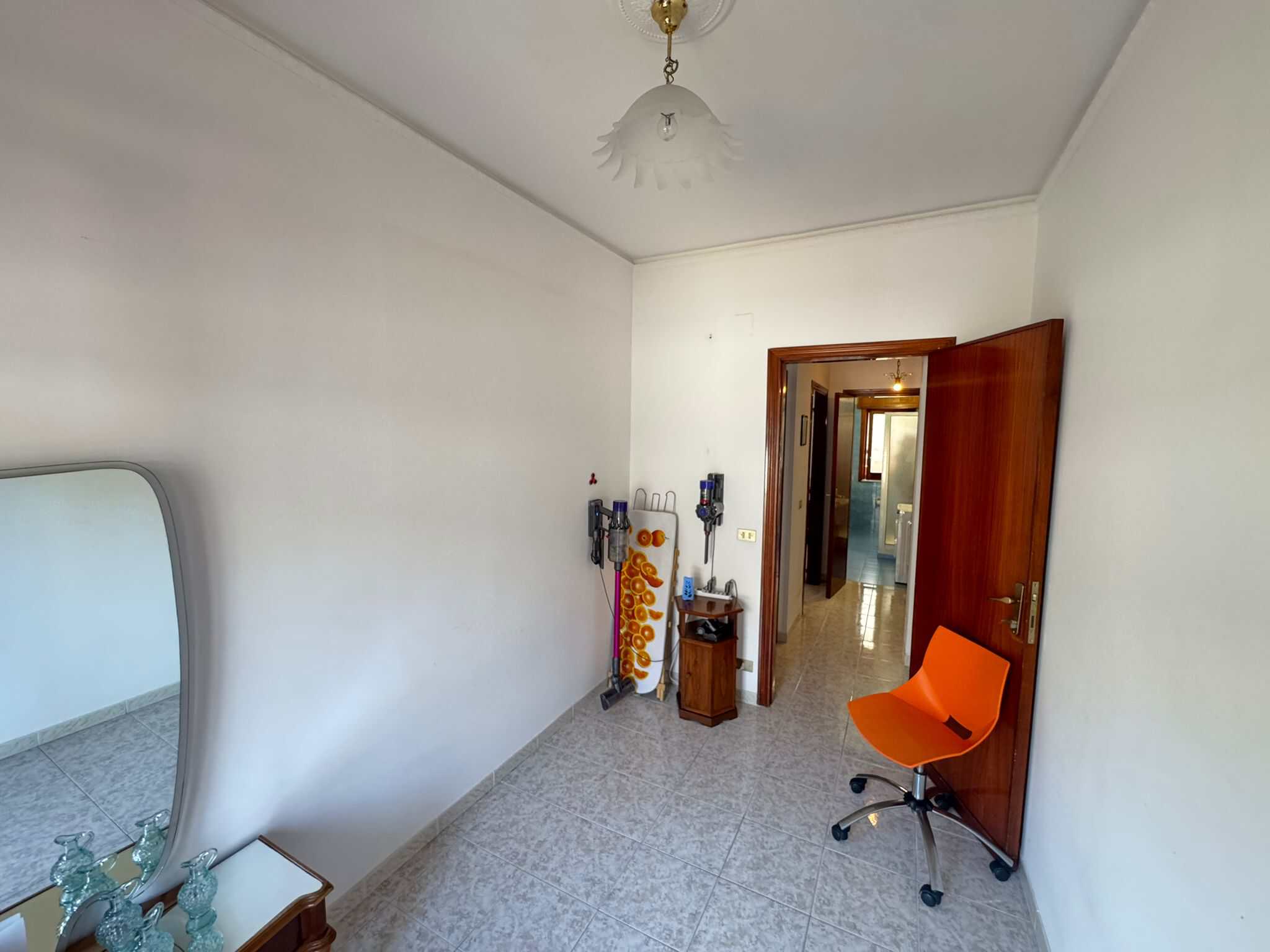 Ampio ingresso con porta in legno, sedia ergonomica arancione e specchio a parete, ideale per ambienti di casa luminosi e funzionali.
