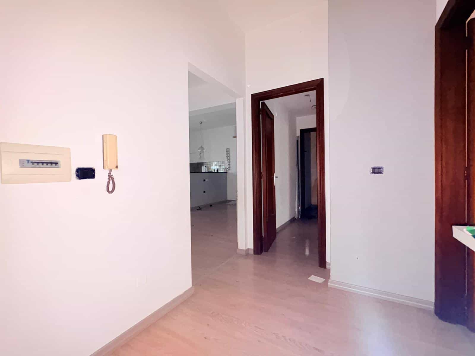 Interno di appartamento moderno con pareti bianche e pavimento in legno chiaro, ingresso e corridoio luminosi, ideale per vendita o affitto immobiliare.