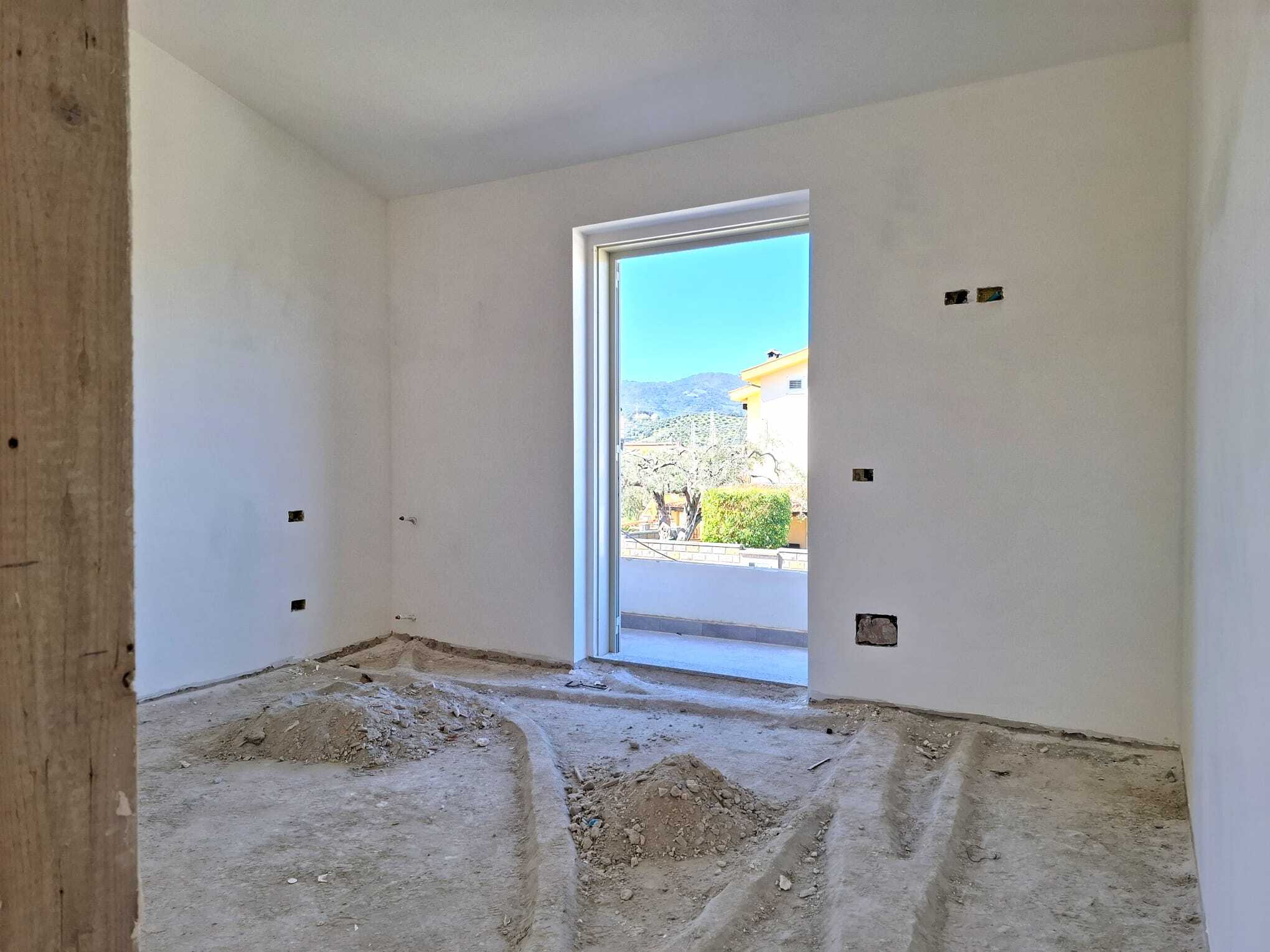 Ampia stanza in fase di ristrutturazione con pareti bianche e grande finestra che offre vista panoramica sulle montagne e sul cielo azzurro.