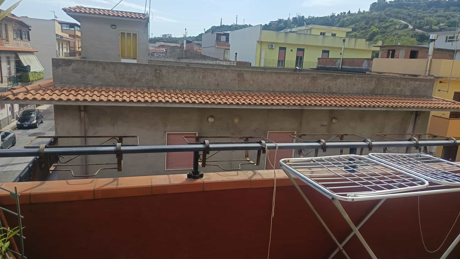 Balcone con stendibiancheria in un quartiere residenziale, vista su edifici colorati e colline sullo sfondo, ideale per servizi di affitto e vendita immobili NextCasa in Italia.