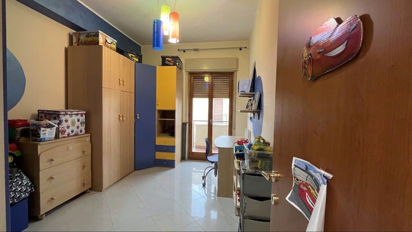 Armadio a muro colorato in camera da letto con spazio di archiviazione e scrivania, illuminata da luce naturale e lampade moderne, ideale per ambienti giovani e dinamici.