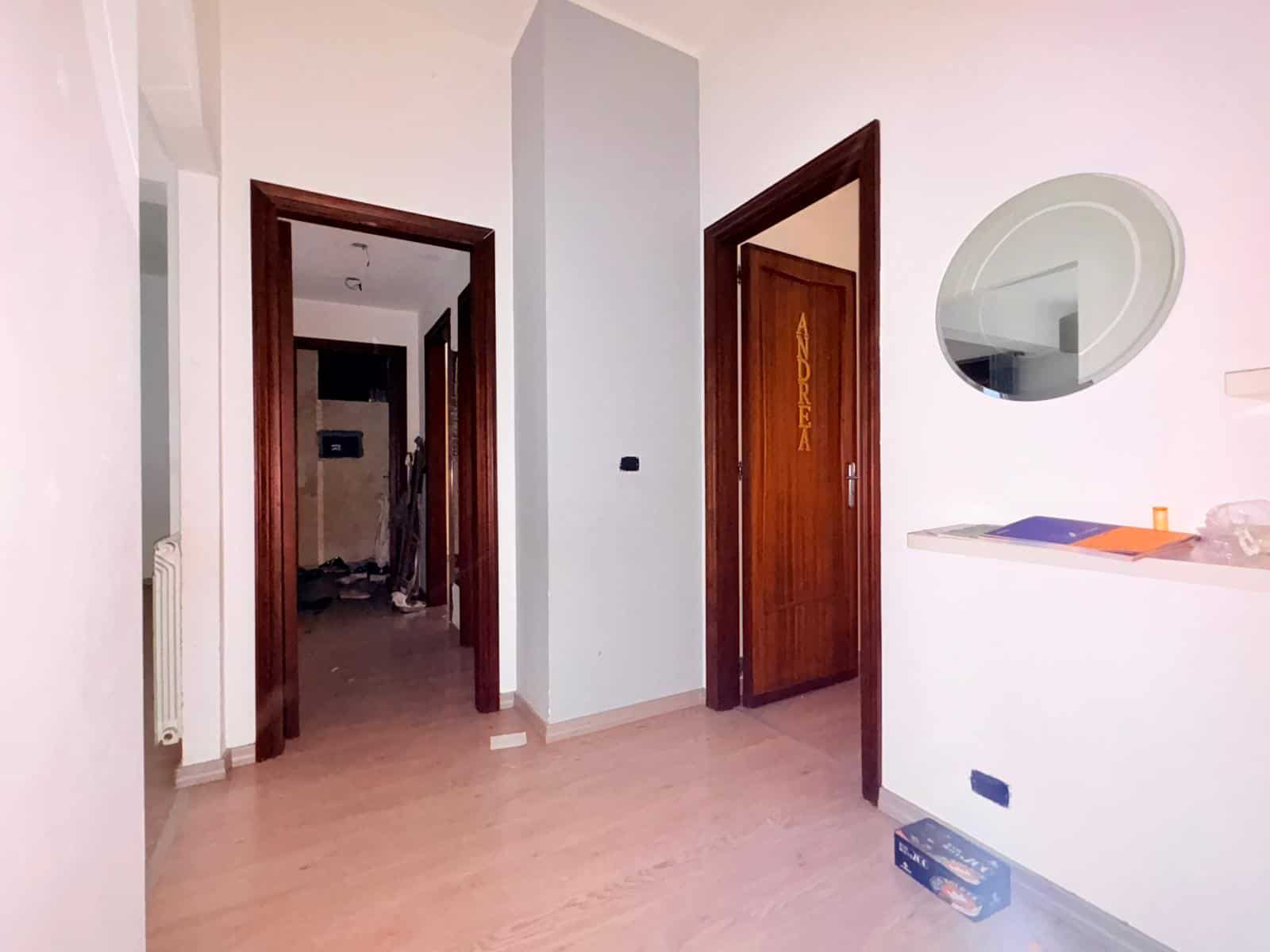 Porte interne in legno e pareti bianche in un ingresso di casa moderna, con specchio rotondo e oggetti decorativi sulla parete, ambiente luminoso e accogliente.