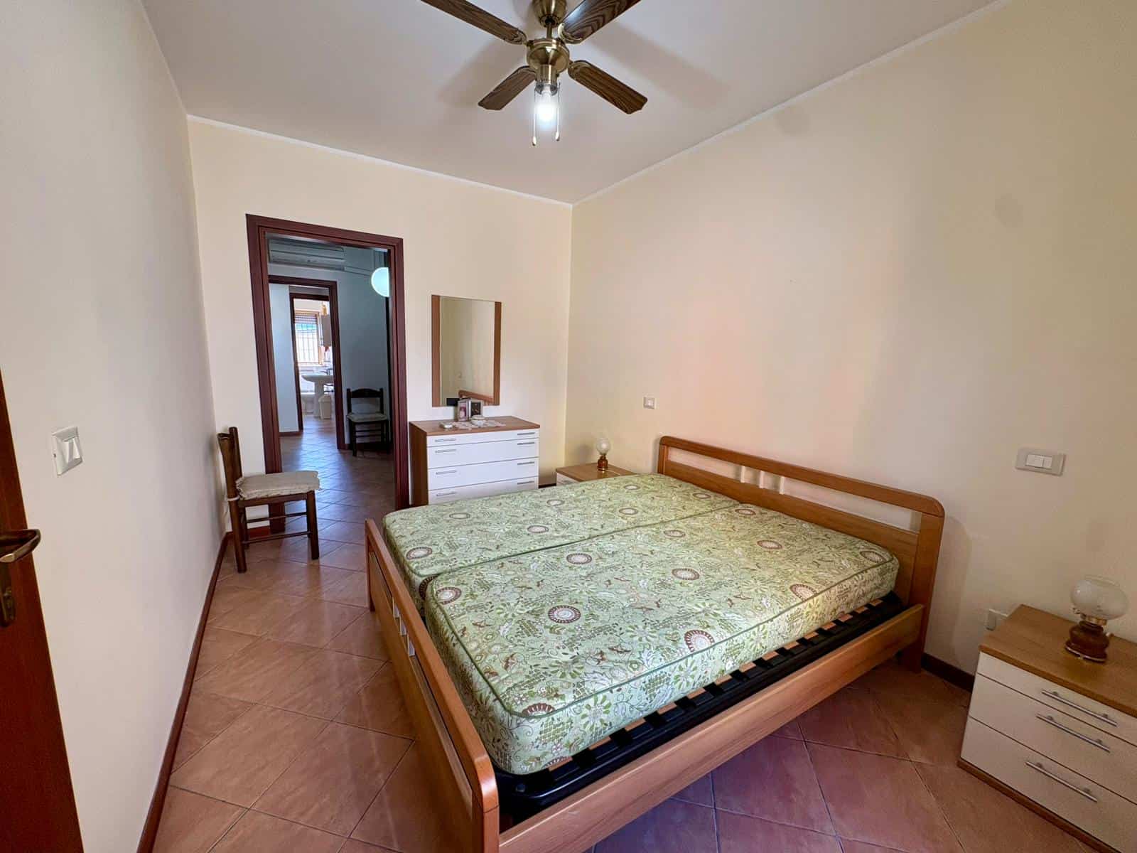 Camera matrimoniale luminosa con letto in legno, comodini e aria condizionata, ideale per affitti turistici o residenziali a NextCasa.