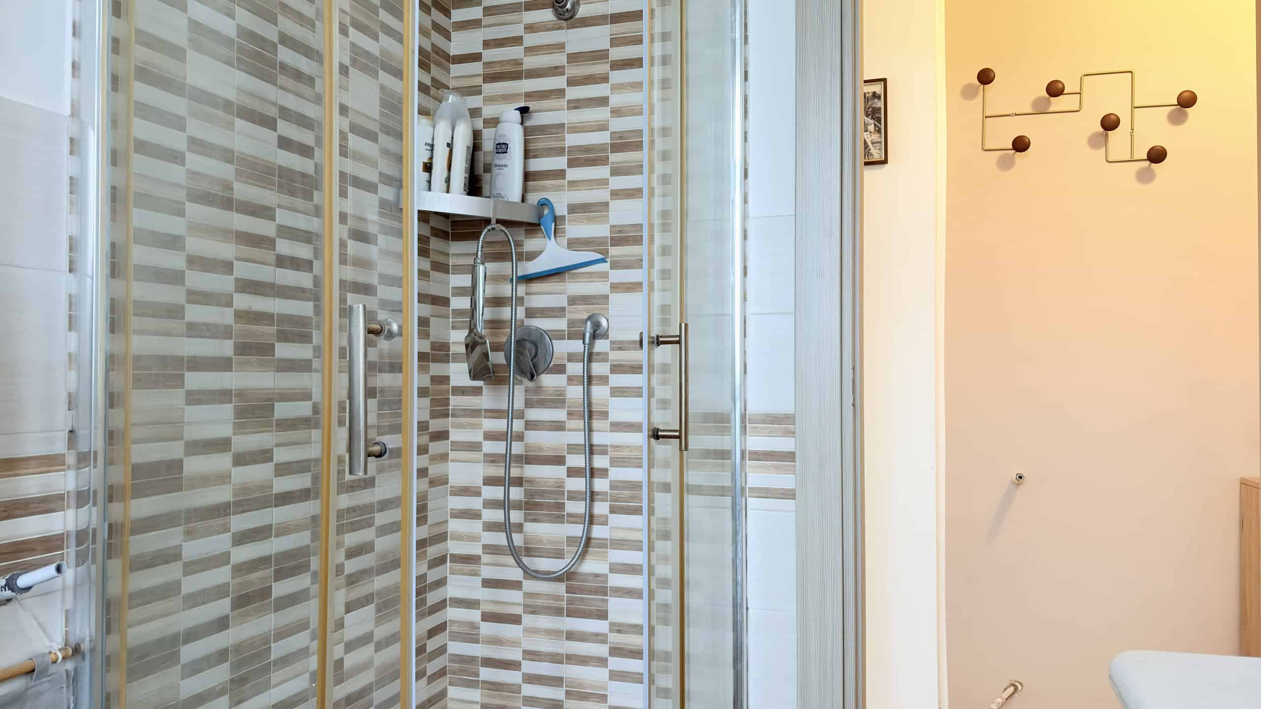 Doccia moderna con pareti in piastrelle beige e accessori per il bagno.