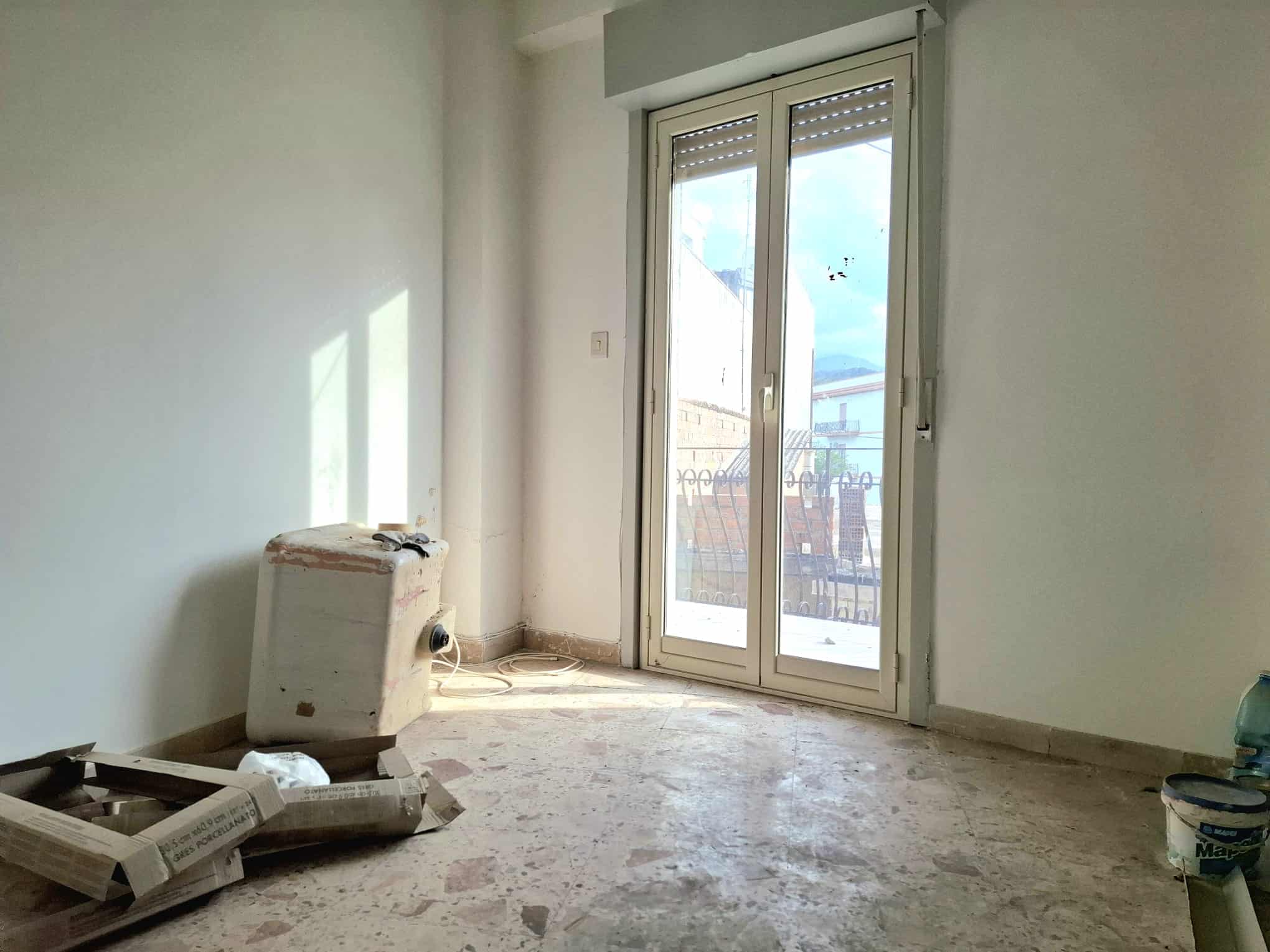 Finestra con balcone in un appartamento in fase di ristrutturazione, luce naturale e vista sulla città, pronto per arredare e personalizzare.