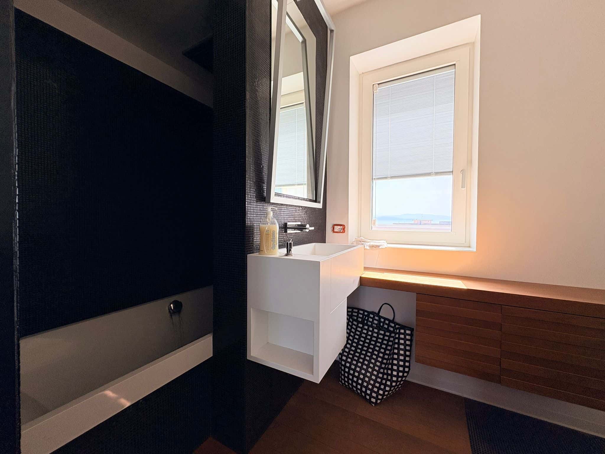 Interno di una camera moderna con finestra luminosa, mobile in legno e specchio, ideale per ambienti di design e comfort.