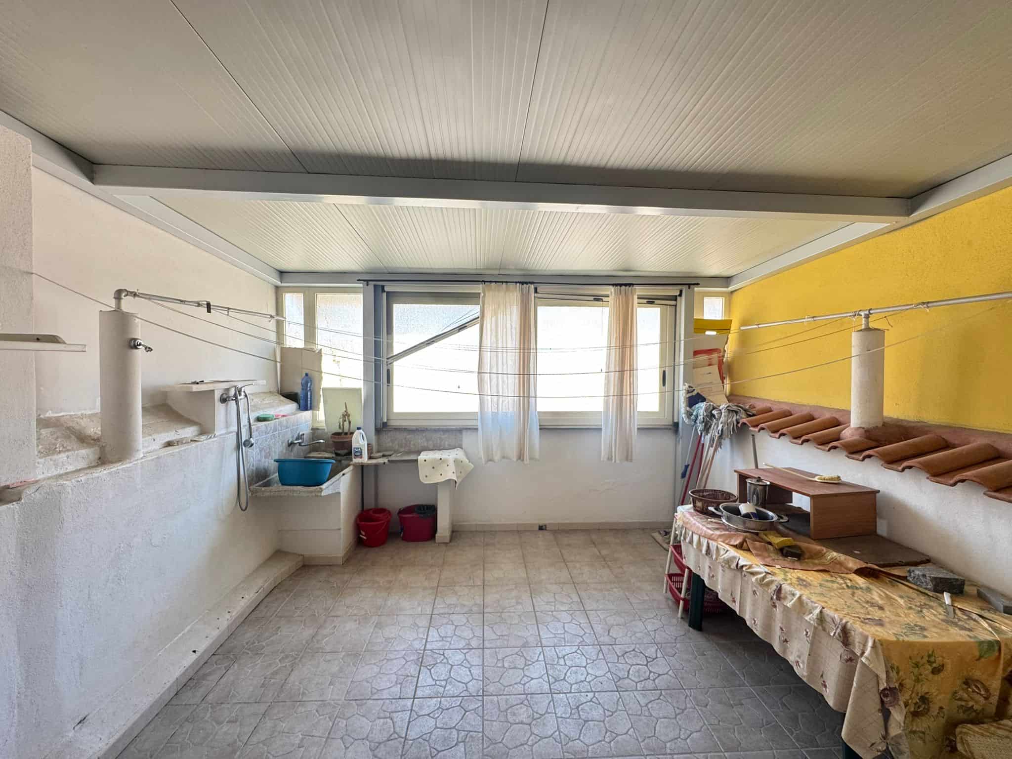 Lavanderia spaziosa con pareti bianche e una parete gialla, dotata di stendibiancheria, lavatrice e spazio per il bucato, ideale per le faccende domestiche e il lavaggio dei vestiti.