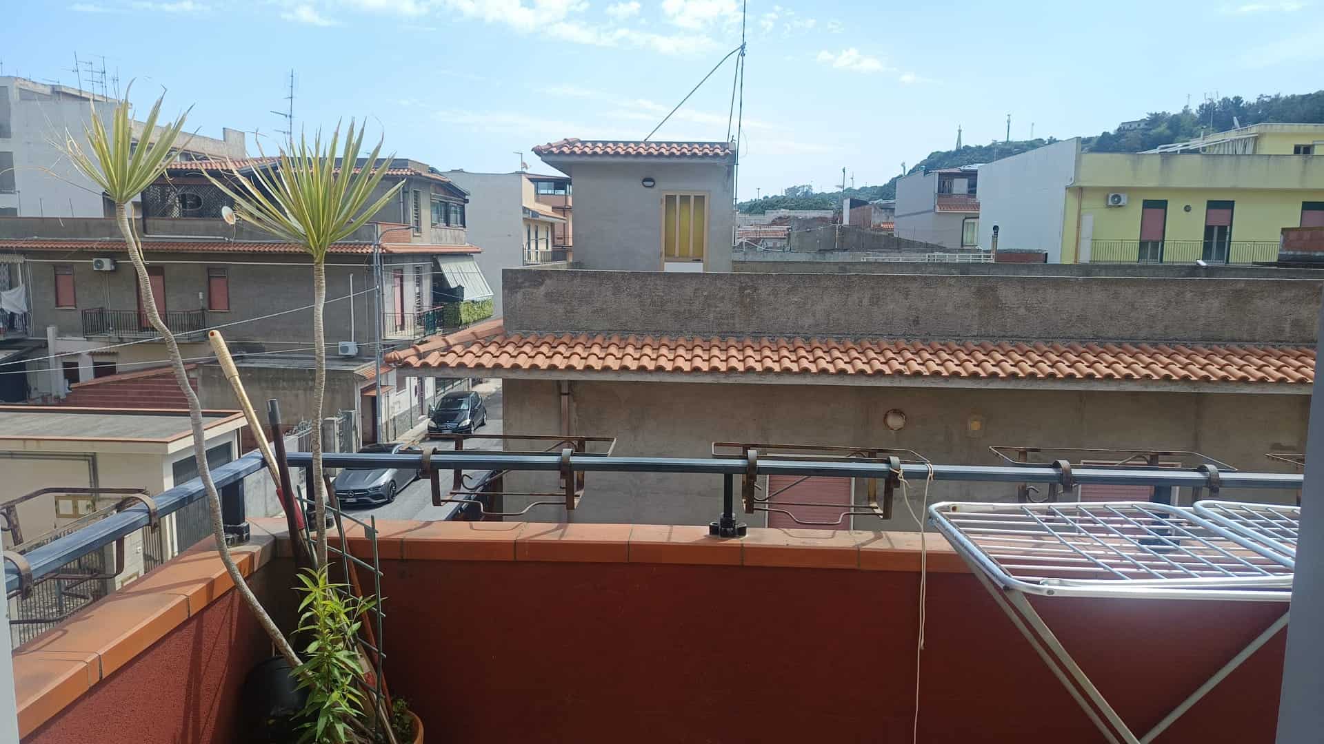 Aggiungi un'immagine di un balcone urbano con piante e vista su edifici residenziali, ideale per annunci immobiliari o proprietà in affitto.