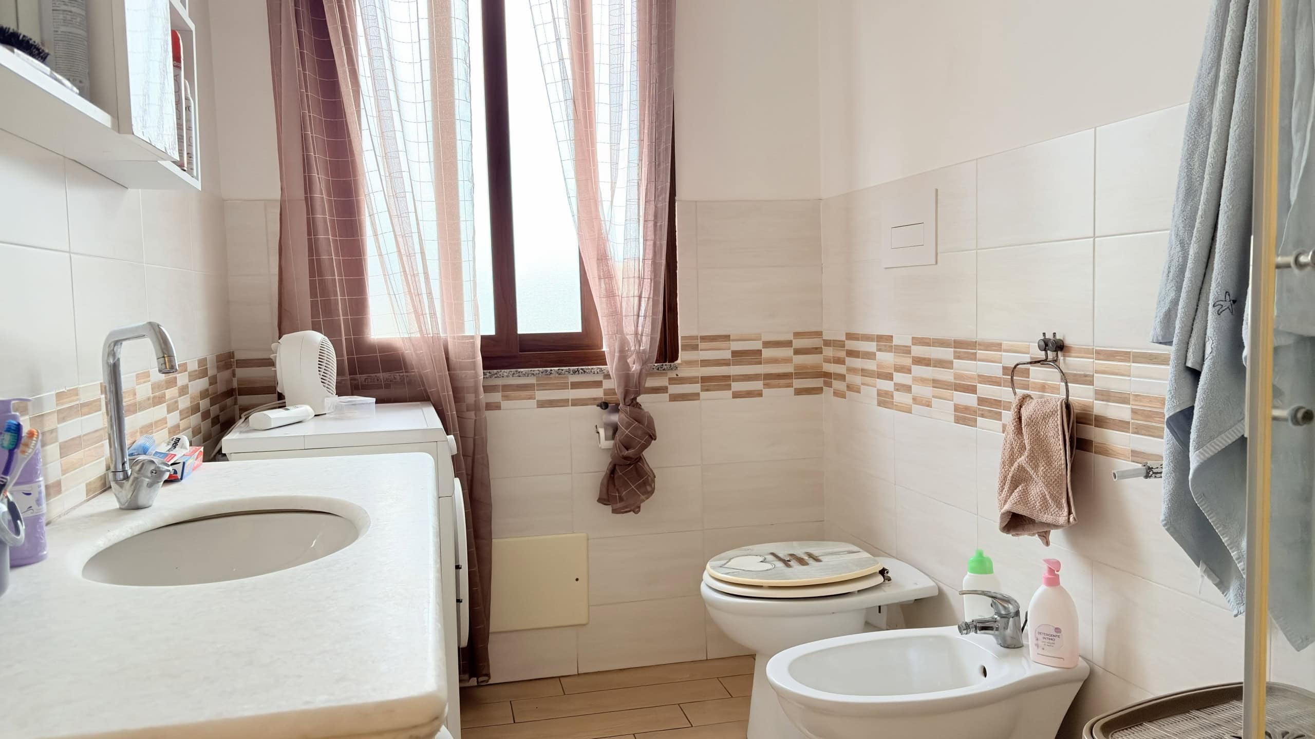Lavatrice e lavabo in bagno luminoso con tende rosa e pareti chiare, ideale per la cura della casa e il comfort quotidiano.