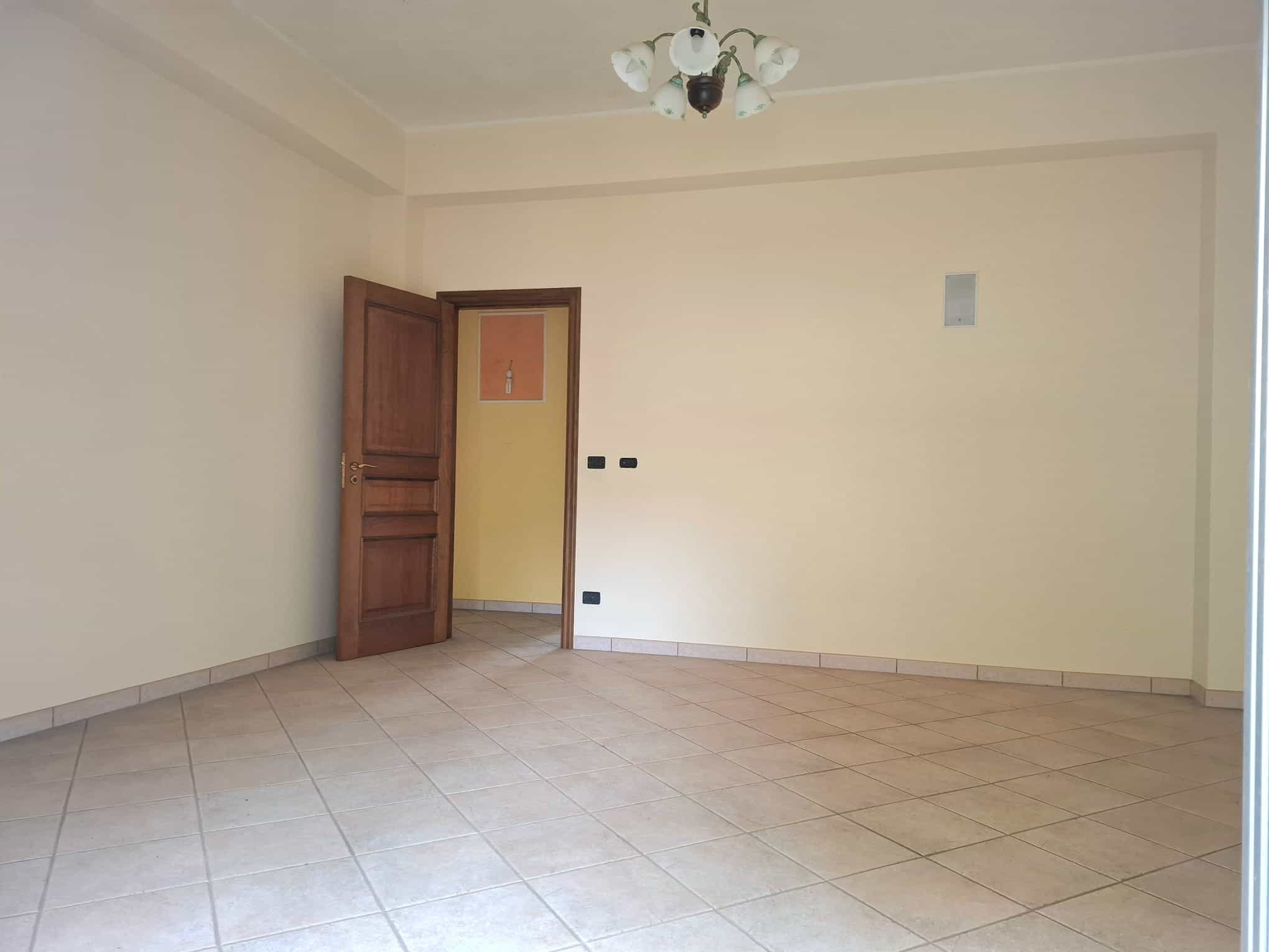 Stanza vuota con pareti beige, pavimento in piastrelle e porta in legno, ideale per arredare o ristrutturare la casa.