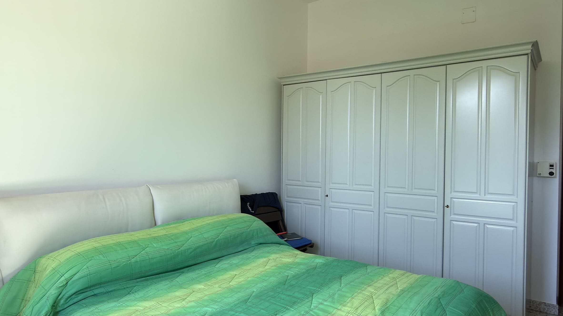 Elegante camera da letto con letto matrimoniale e grande armadio a muro bianco, ambiente luminoso e accogliente, ideale per soggiorni confortevoli e rilassanti.
