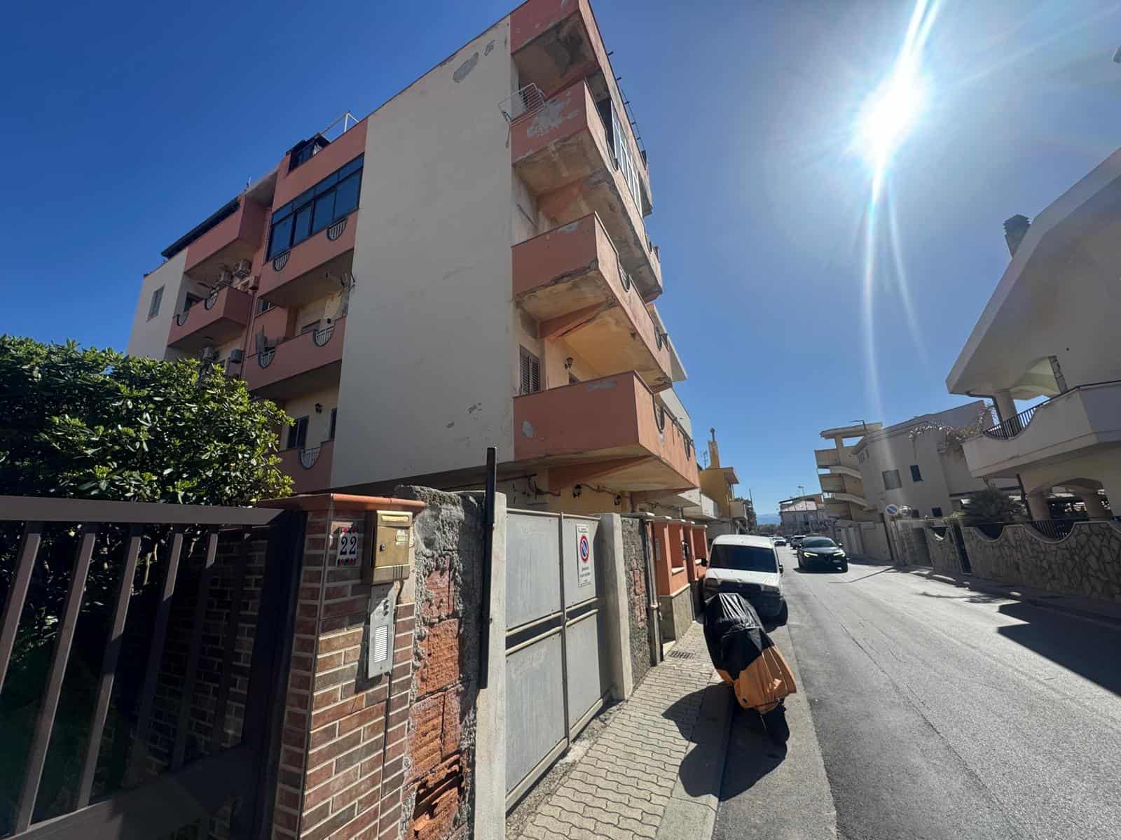Balcone di un appartamento in un edificio residenziale con vista sulla strada soleggiata, in un quartiere urbano di città italiane, con edifici moderni e cielo sereno.